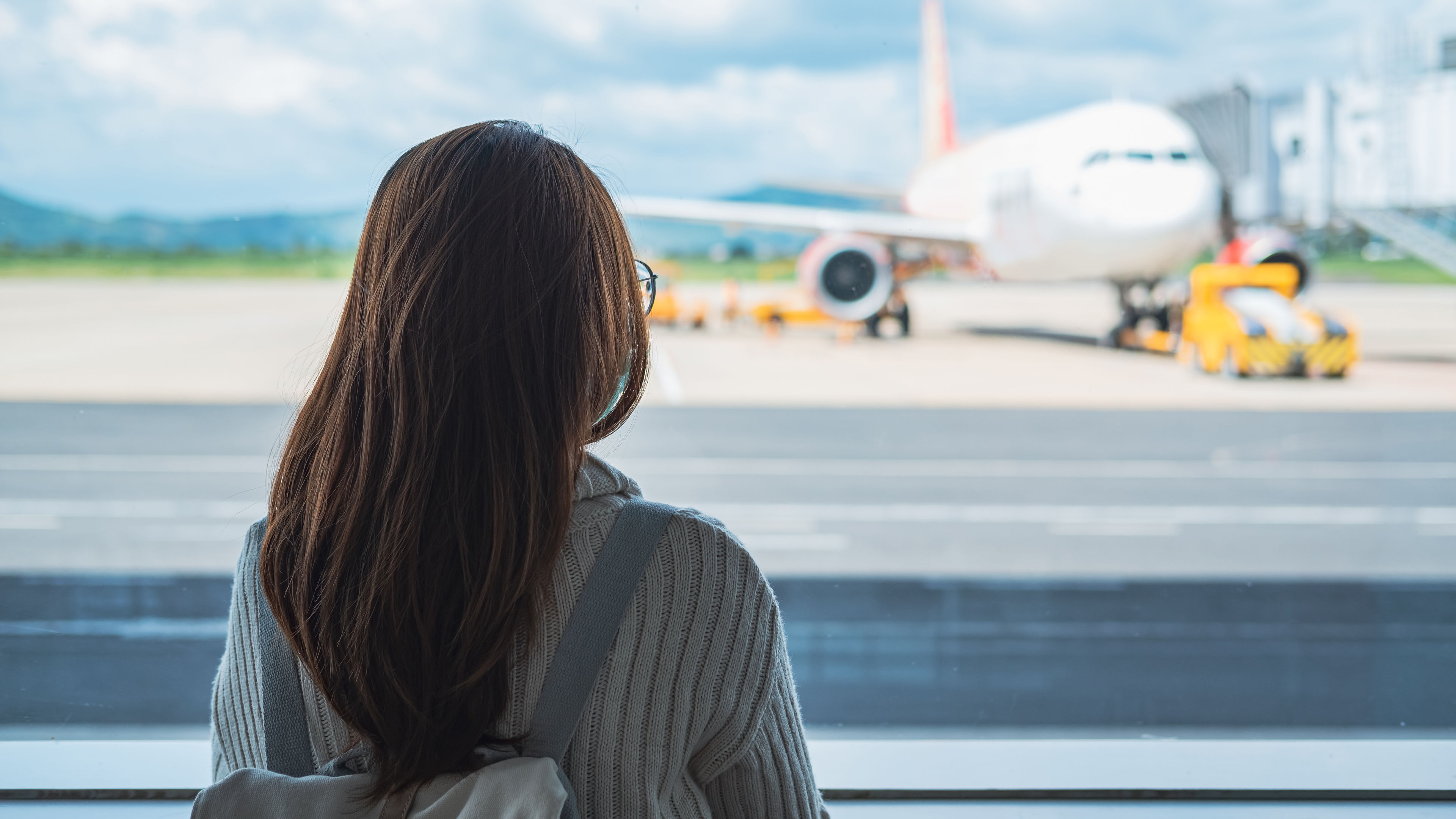 Rear view of a woman with a backpack looking at a plane through an airport window