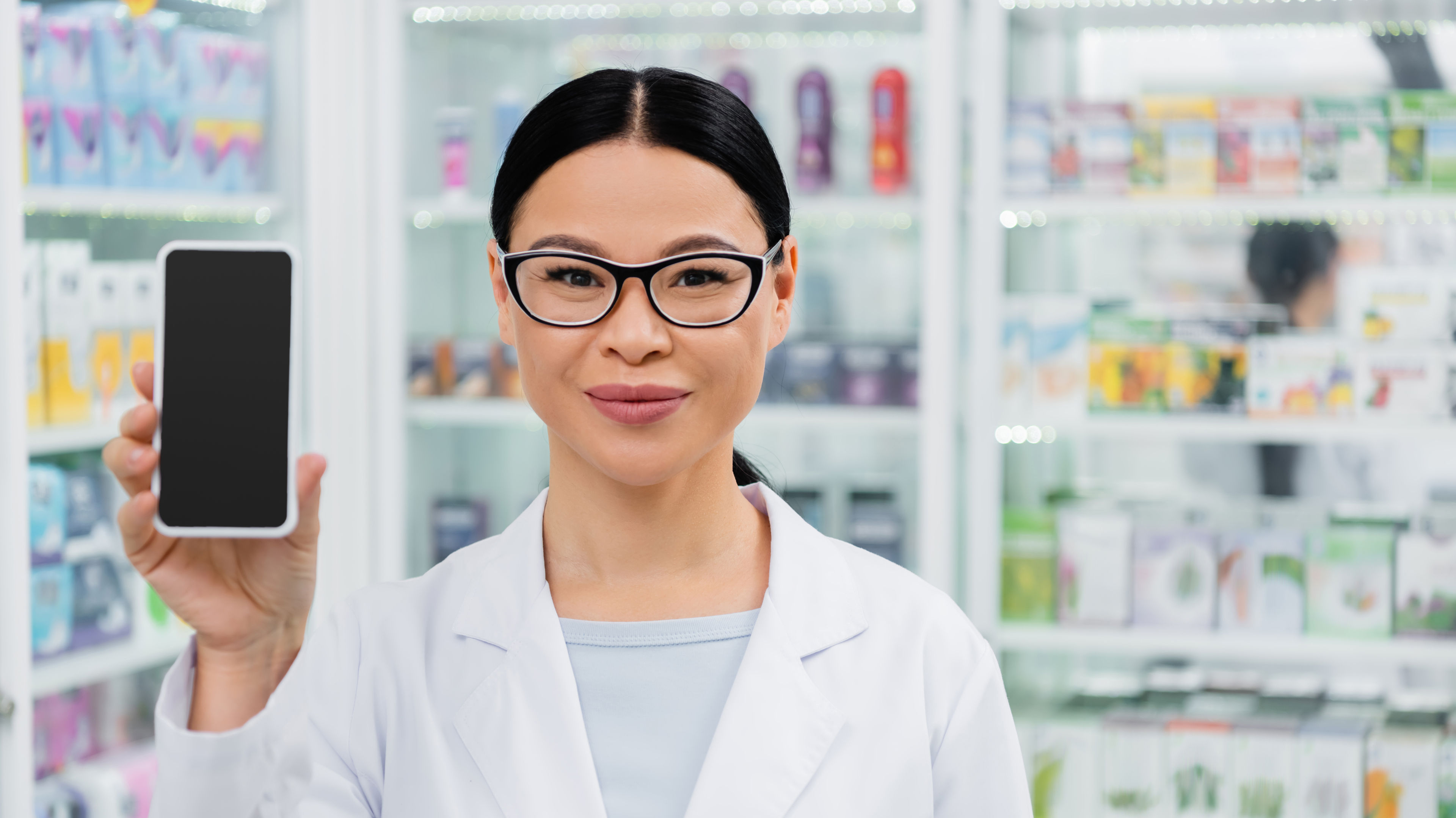 A young pharmacist smiling with a smartphone in hand 