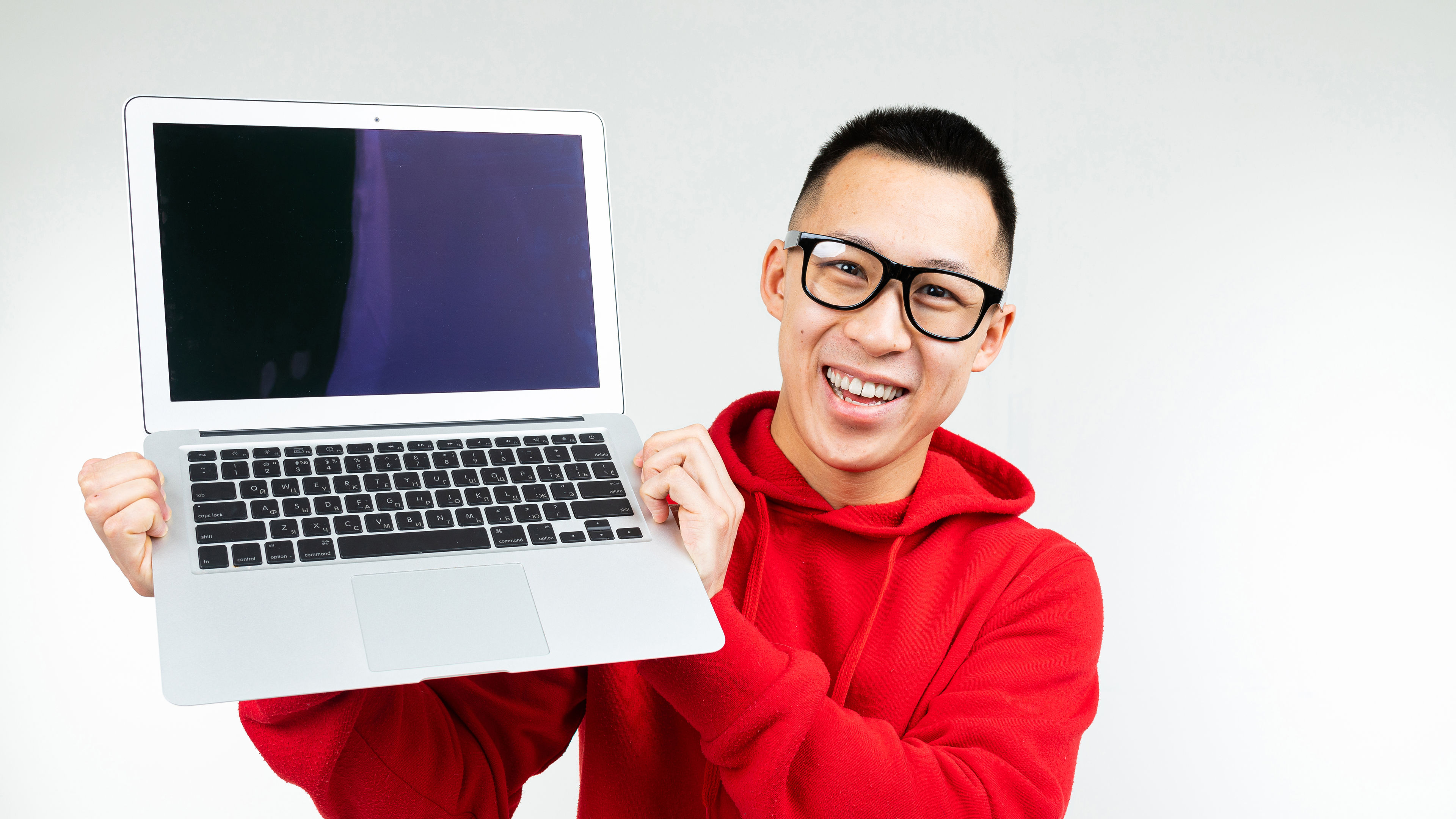 Asian man shows laptop screen with mockup on white studio background 