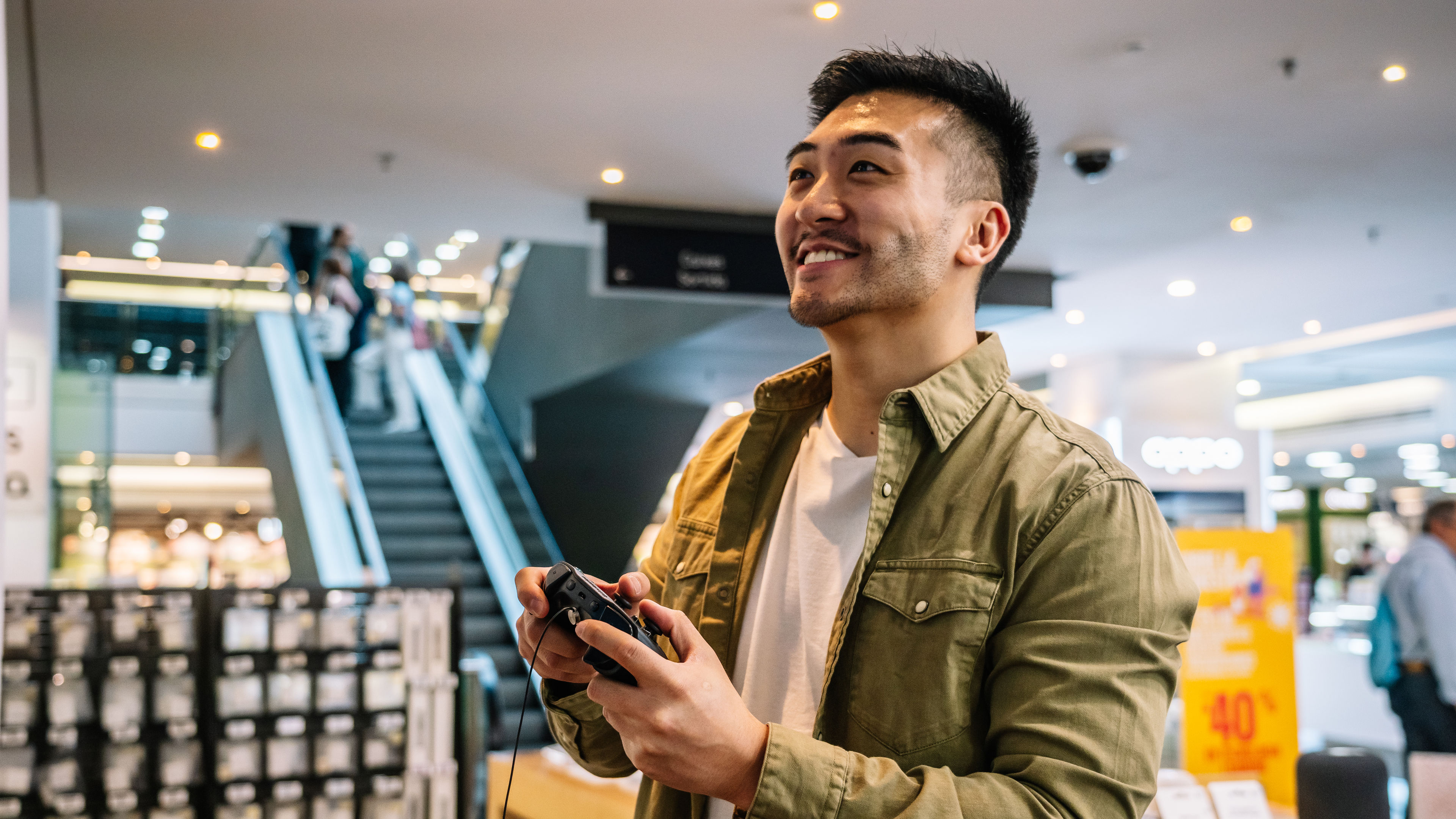  Happy Asian man playing videogame with joystick in mall 