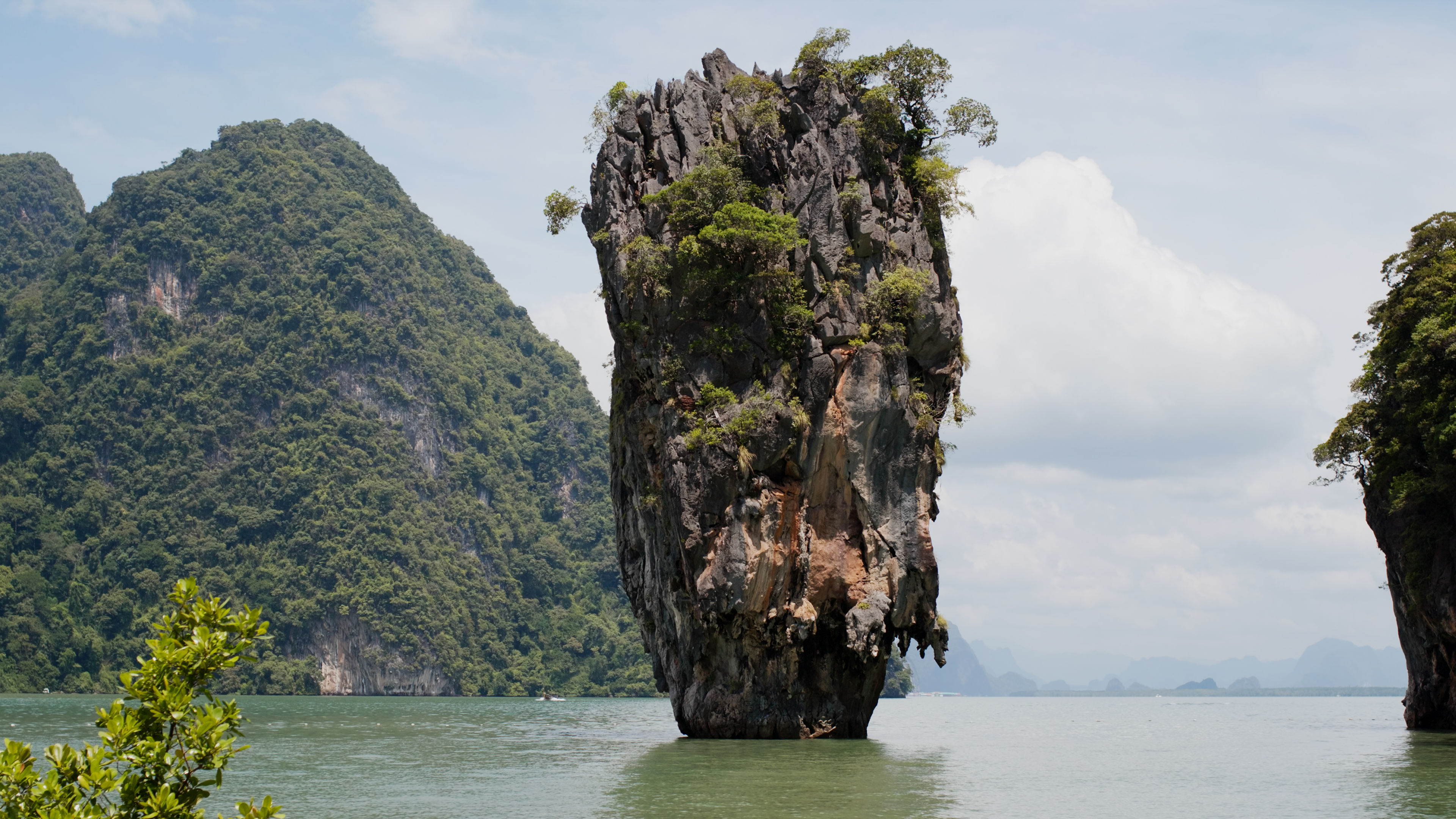 Majestic limestone karst rising from the emerald waters of Phang Nga Bay, Thailand, surrounded by lush green cliffs and a serene tropical landscape. 