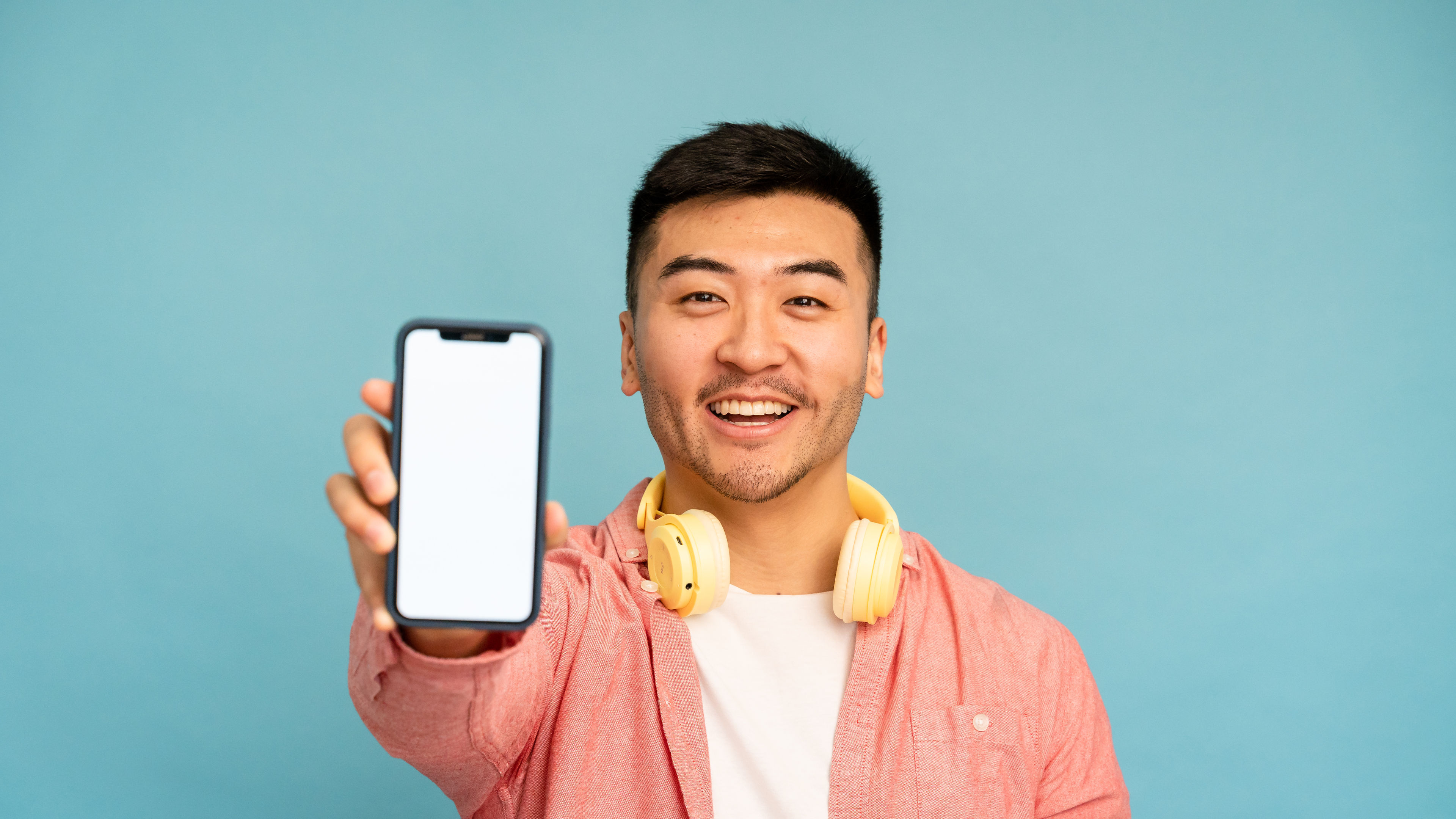 Smiling young man showing blank cell phone screen in a blue background 