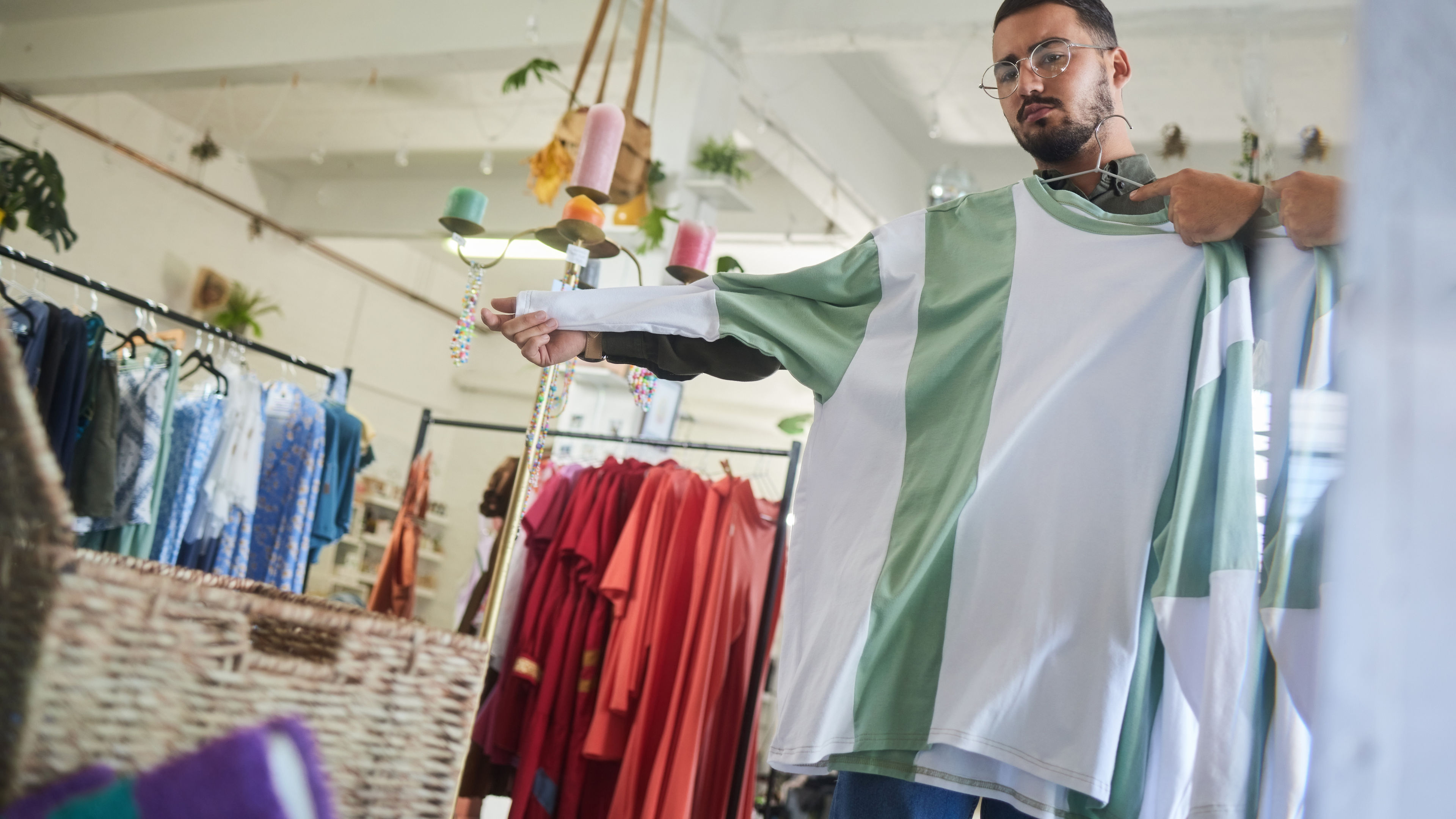 A man with glasses checking out T-shirt in front of a mirror.
