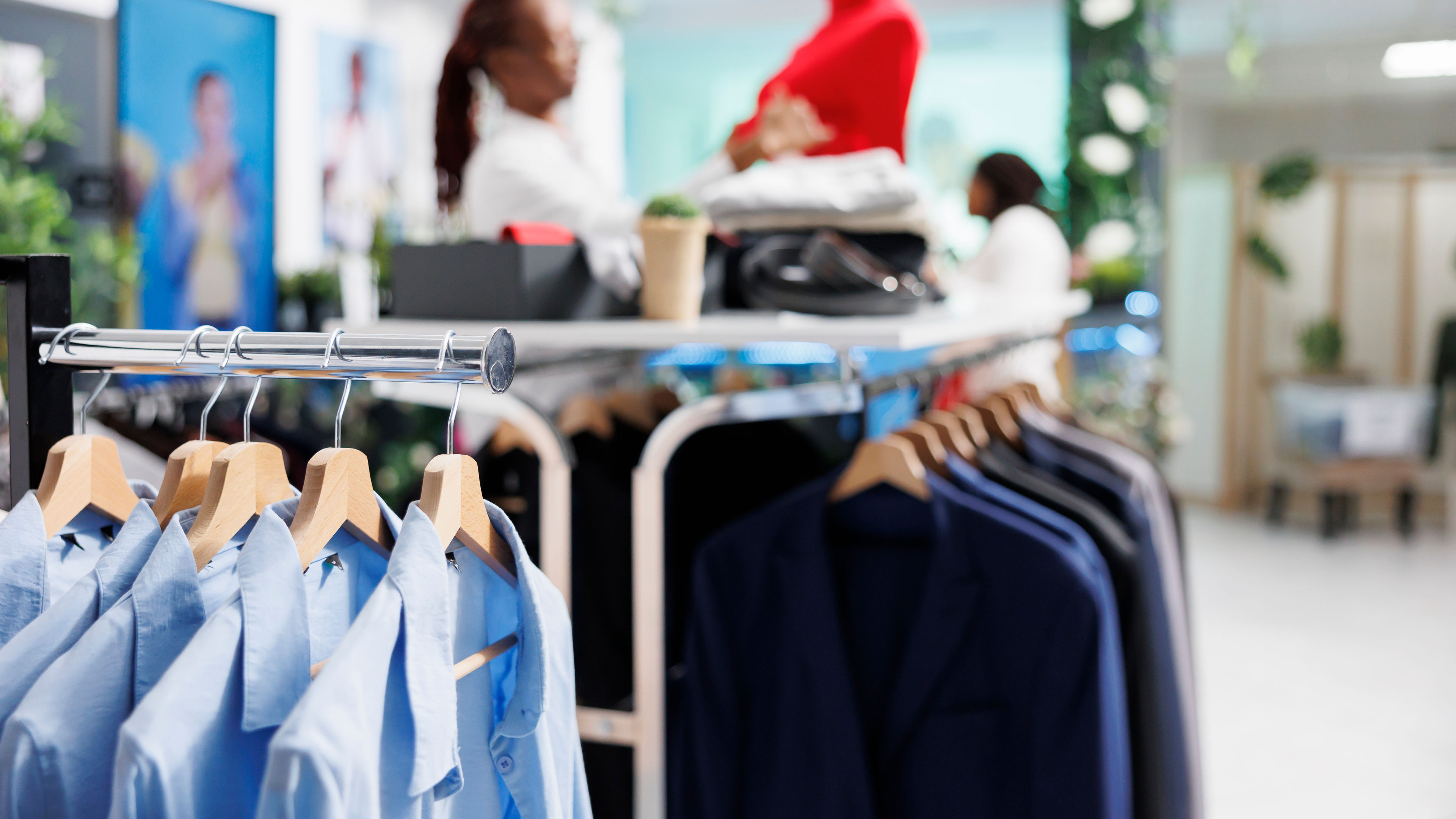 A variety of men's shirts neatly arranged on display in a clothing store, with a female salesperson blurred in the background.