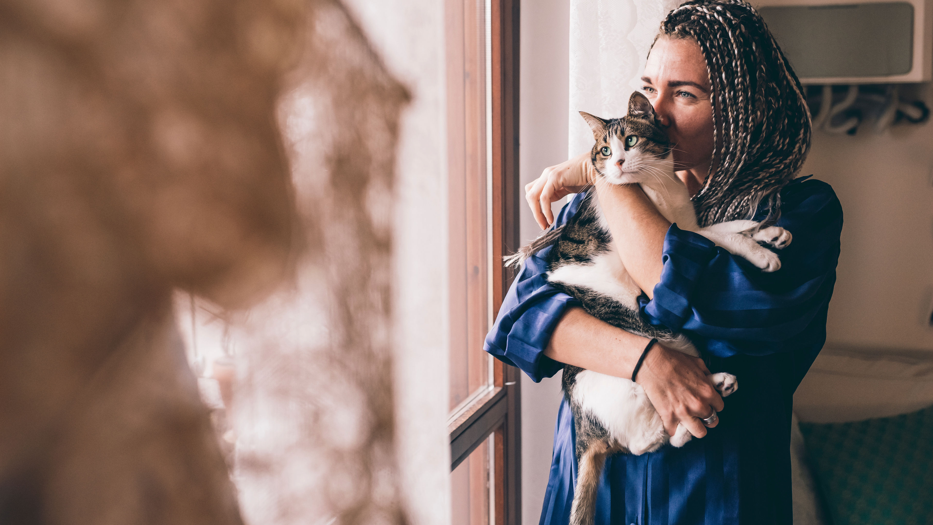 A woman in a blue robe holds her cat near a window 