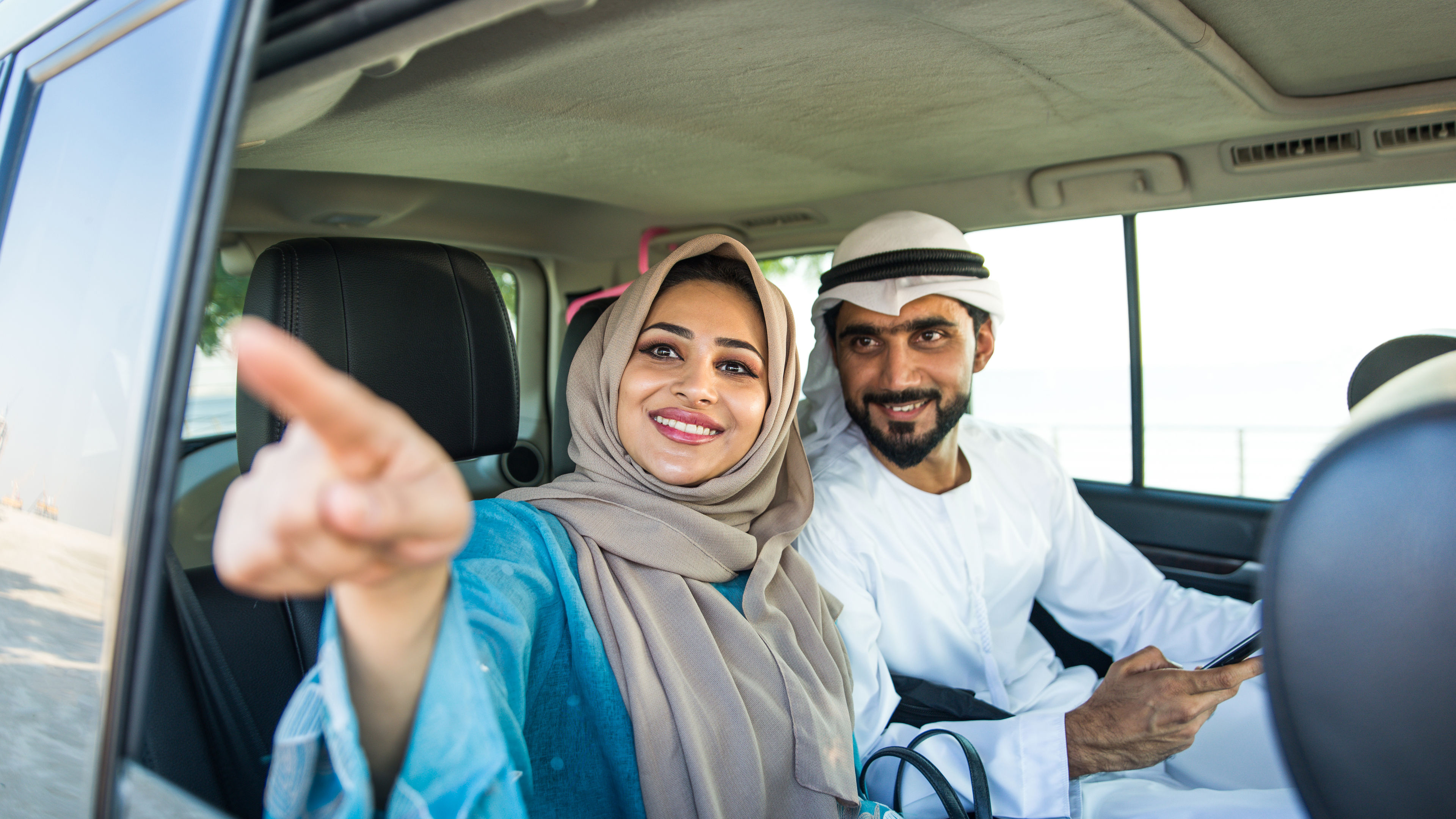 زوجان عربيان يستمتعان برحلتهما أثناء القيادة في سيارة معا. 