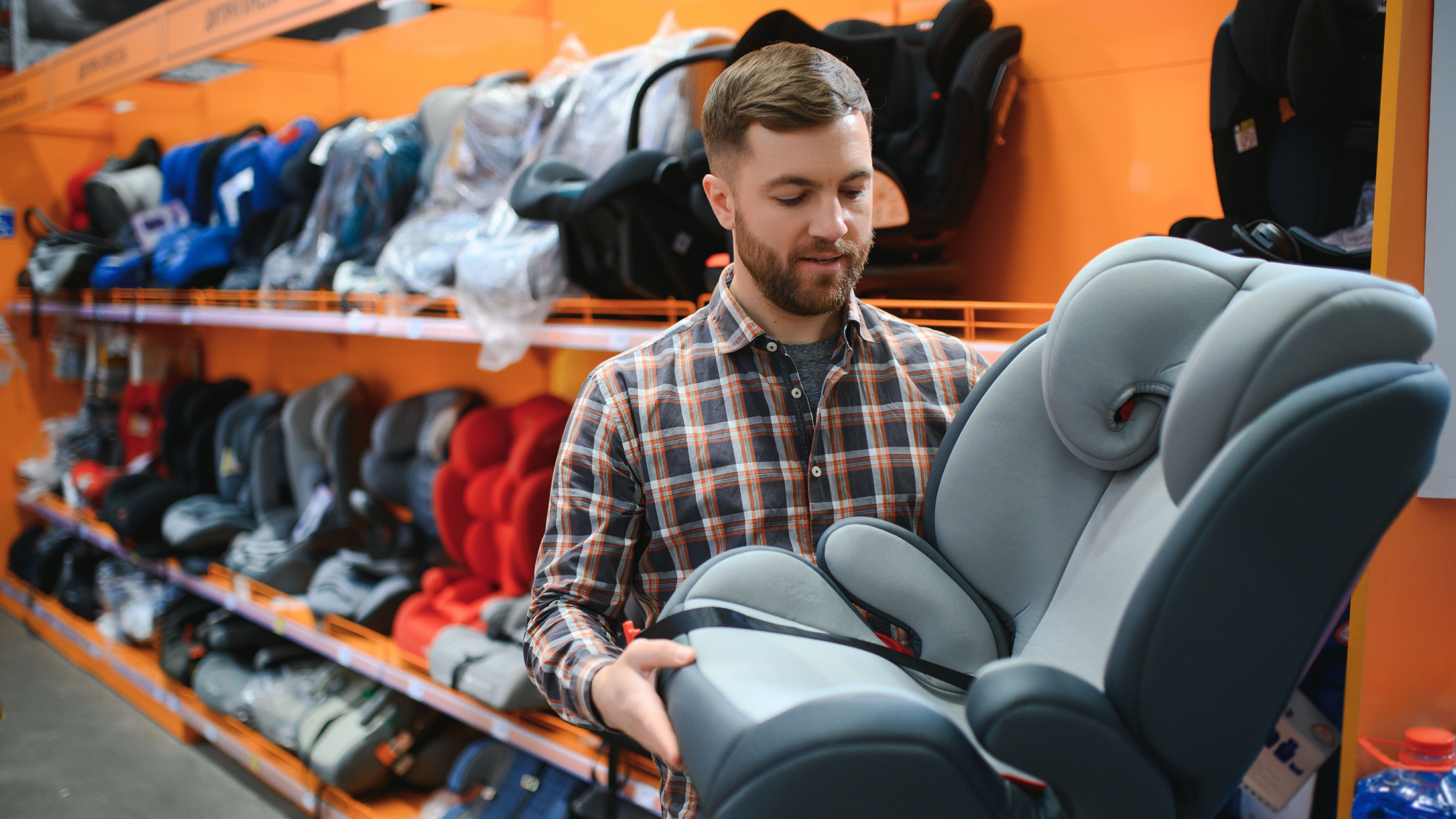 Young male with car seat for kids in the children's store.