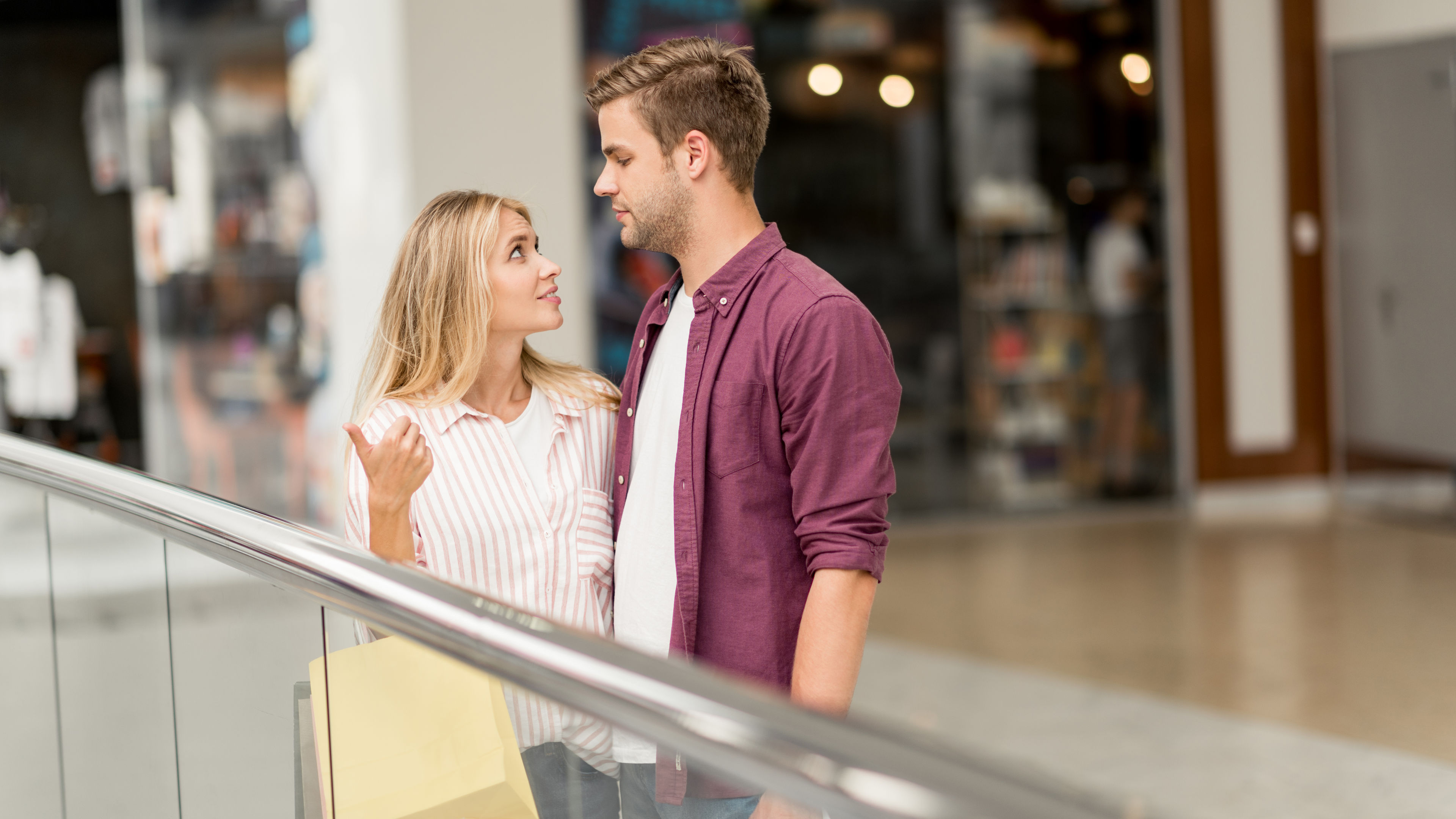 A beautiful young woman holding shopping bags pointing at her boyfriend in a shopping mall 