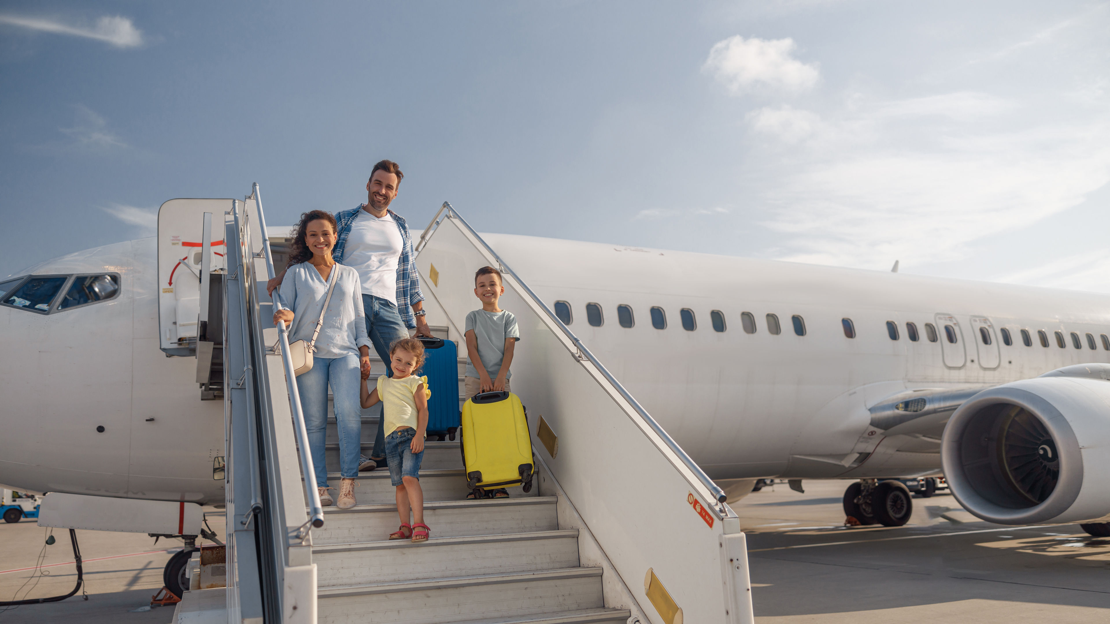 A cheerful family of four is stepping off an airplane with luggage.