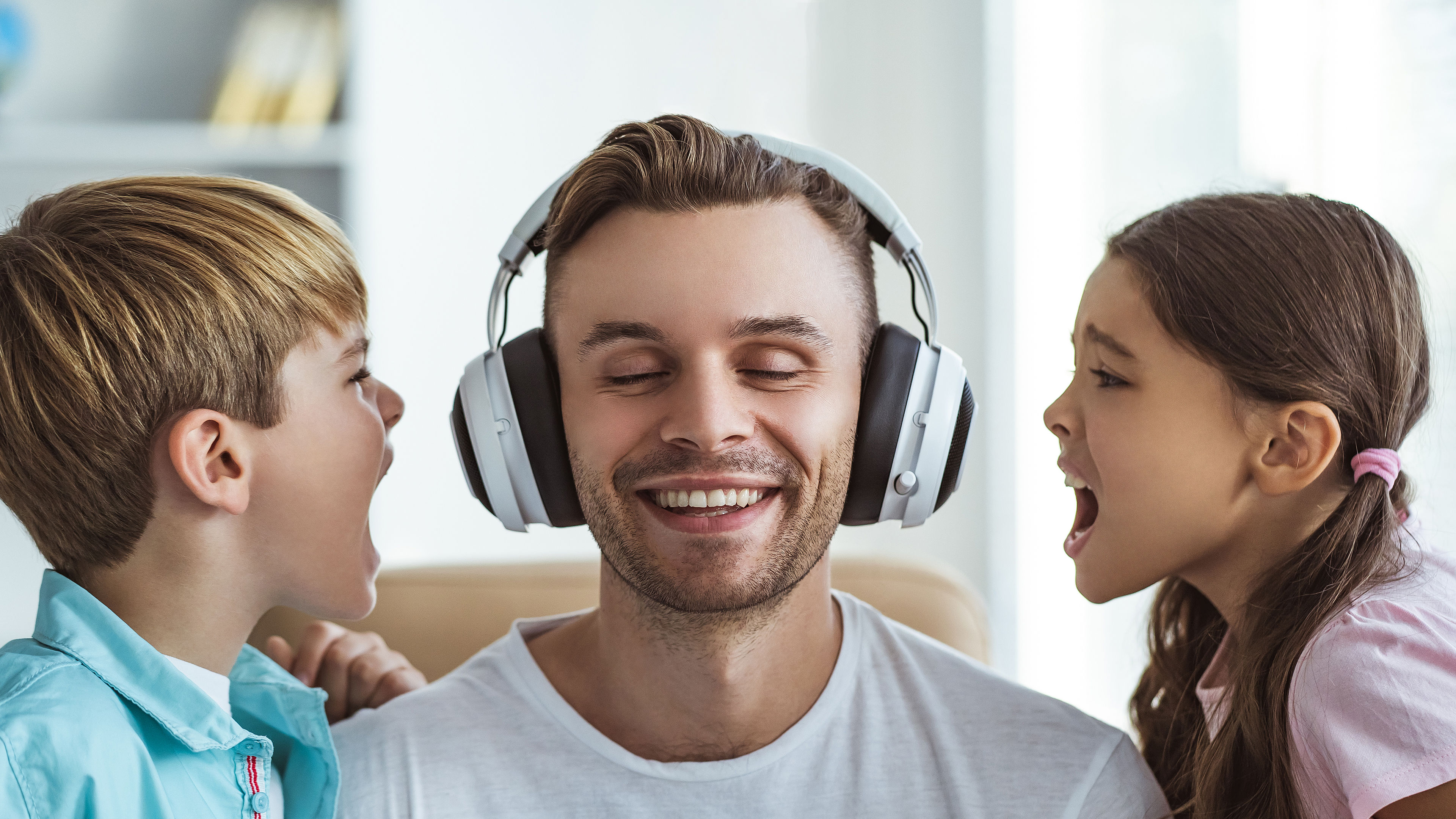 A joyful father, wearing headphones, shares a playful moment with his young son and daughter 