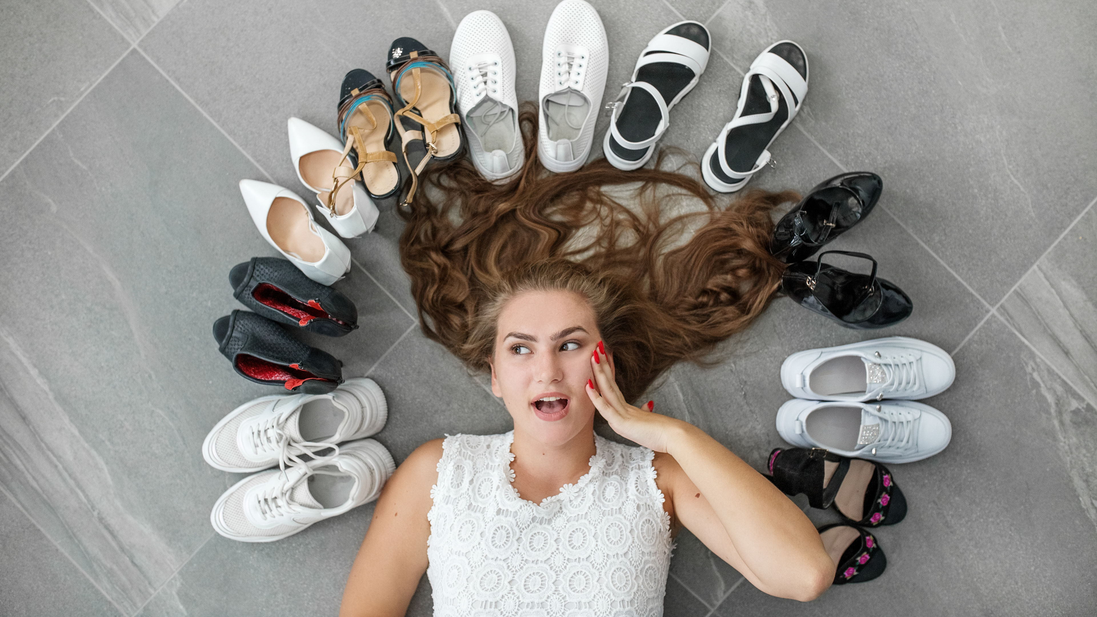 A cheerful woman beams with excitement as she admires a wide selection of women's shoes spread out around her 