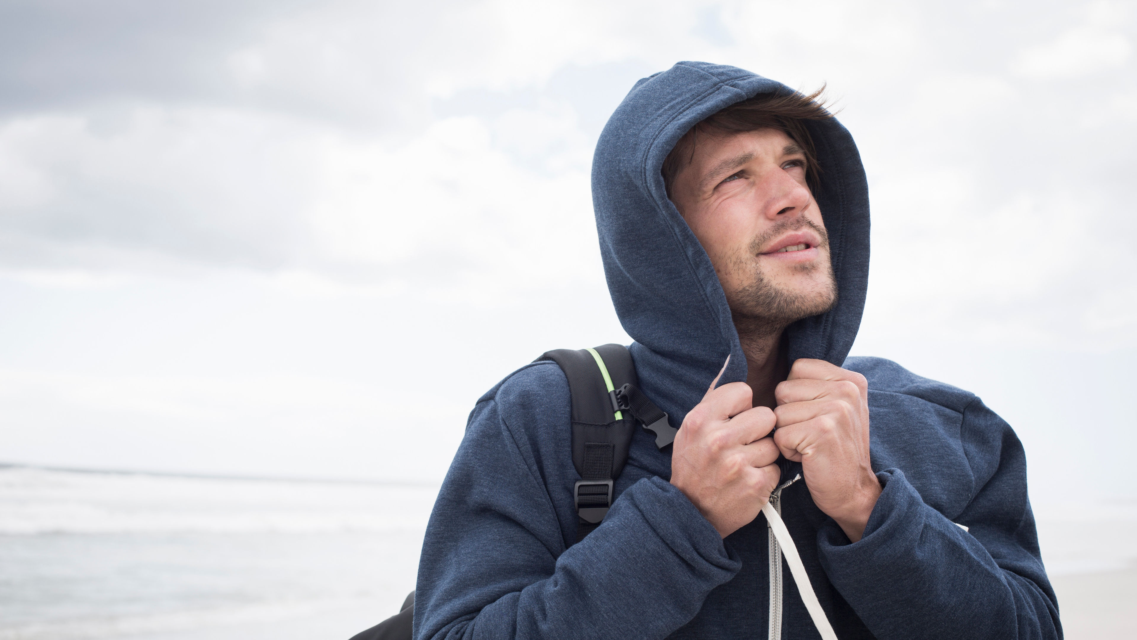 A man wearing a navy-blue hoodie and carrying a backpack 