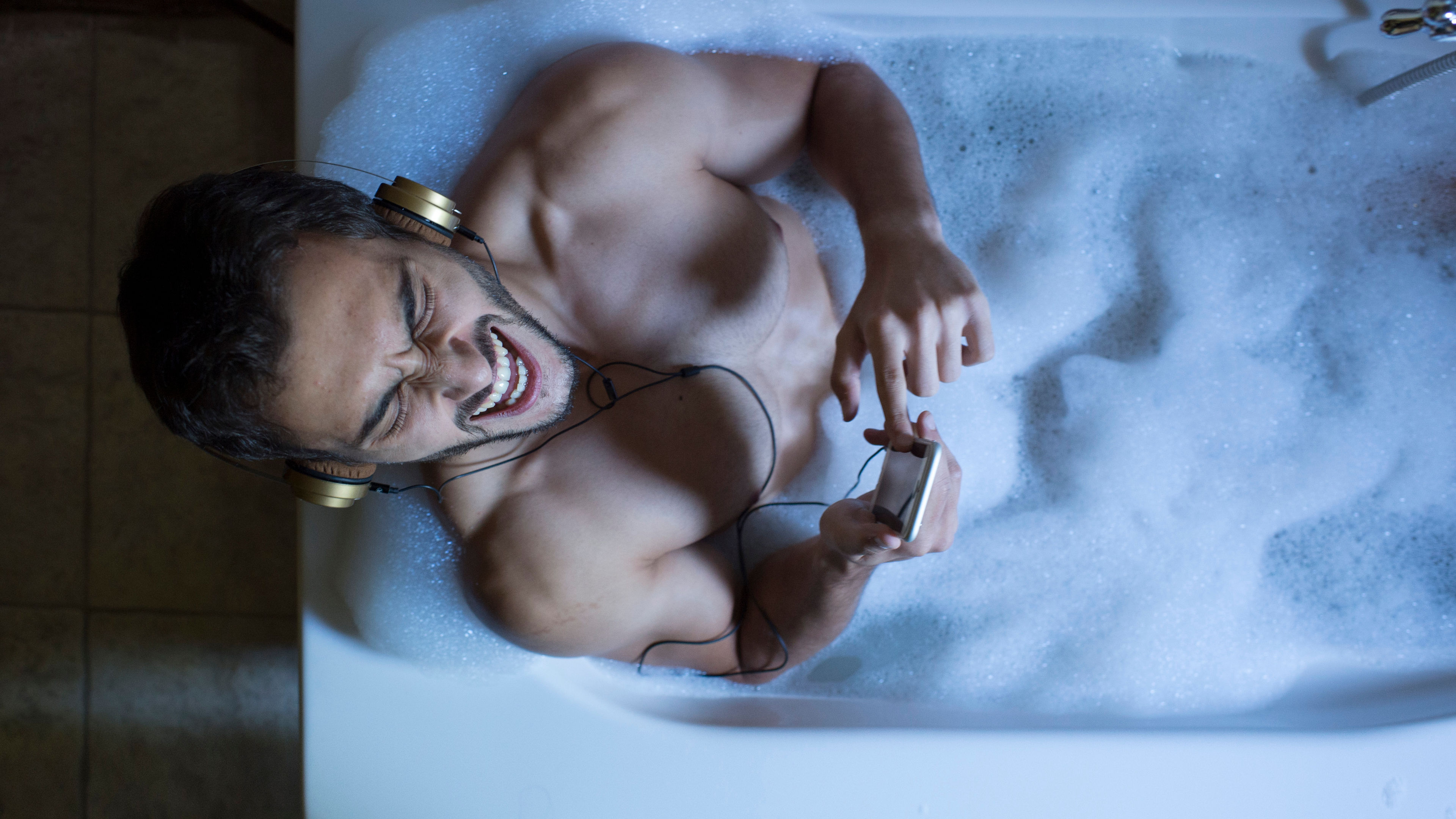 A happy man in a shower with headphones in ear 