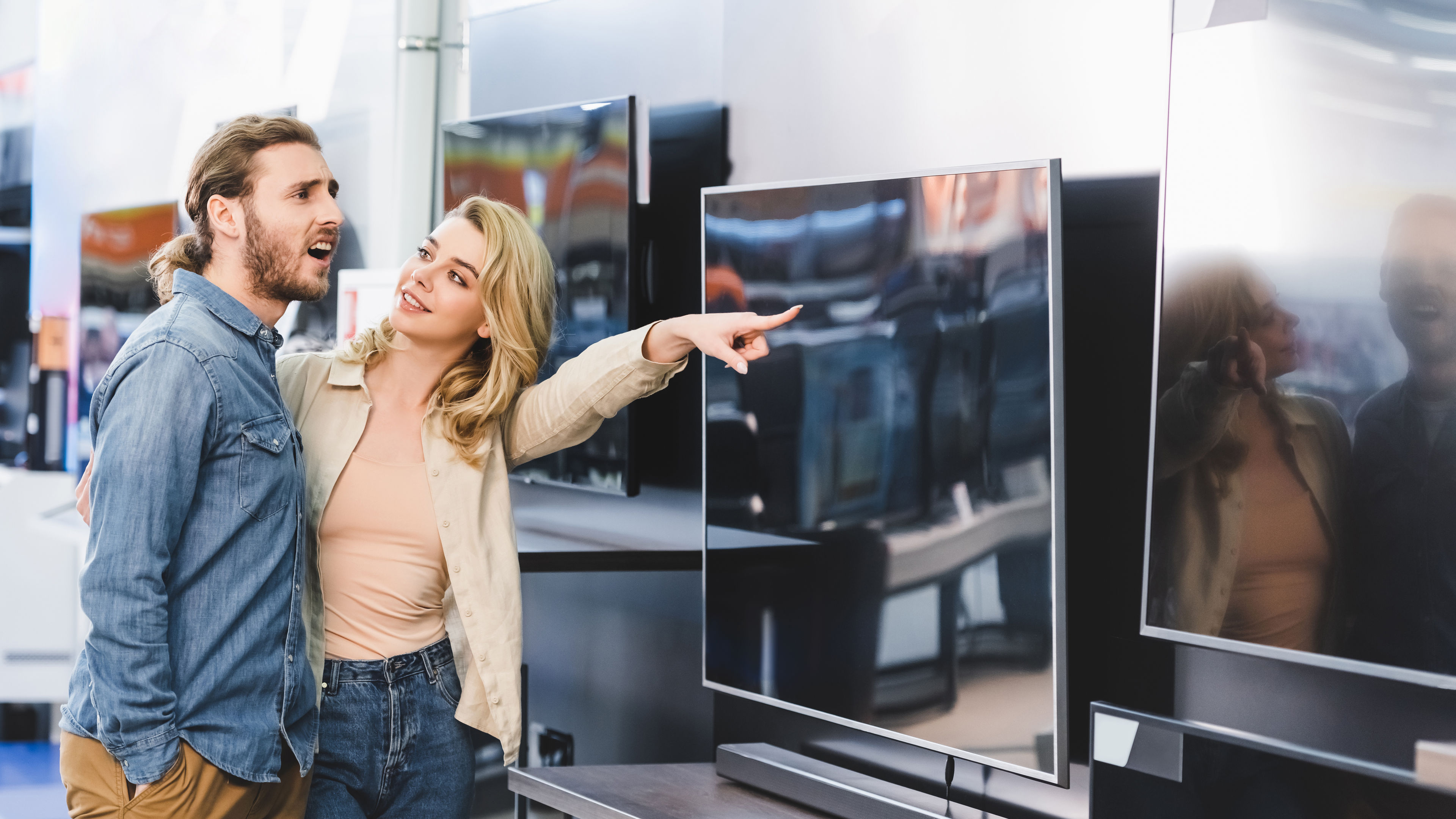 A smiling girlfriend enthusiastically pointing at a TV, sharing her excitement 