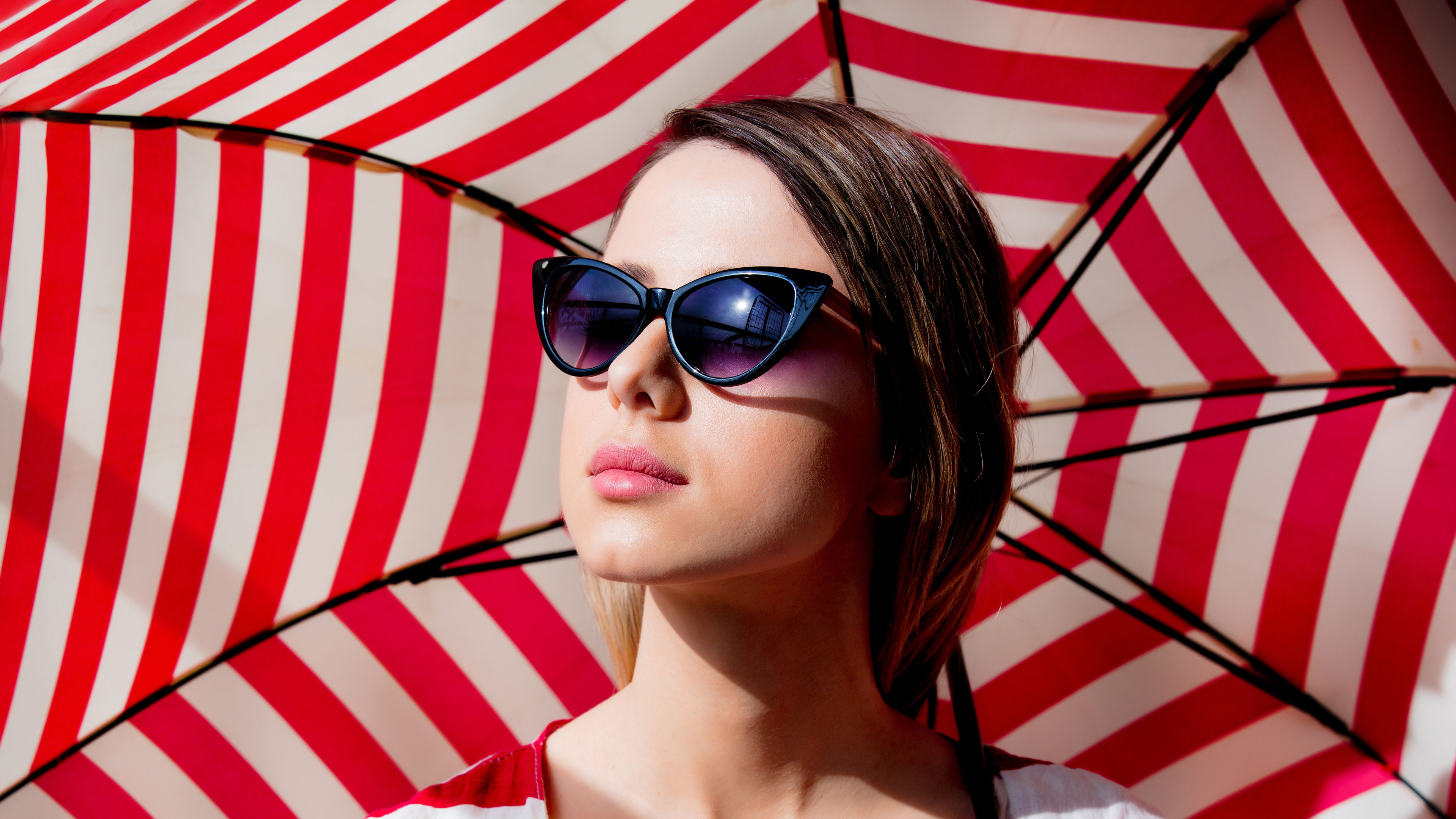 A stylish redhead stands confidently, holding a red-striped umbrella that complements her bold look. 