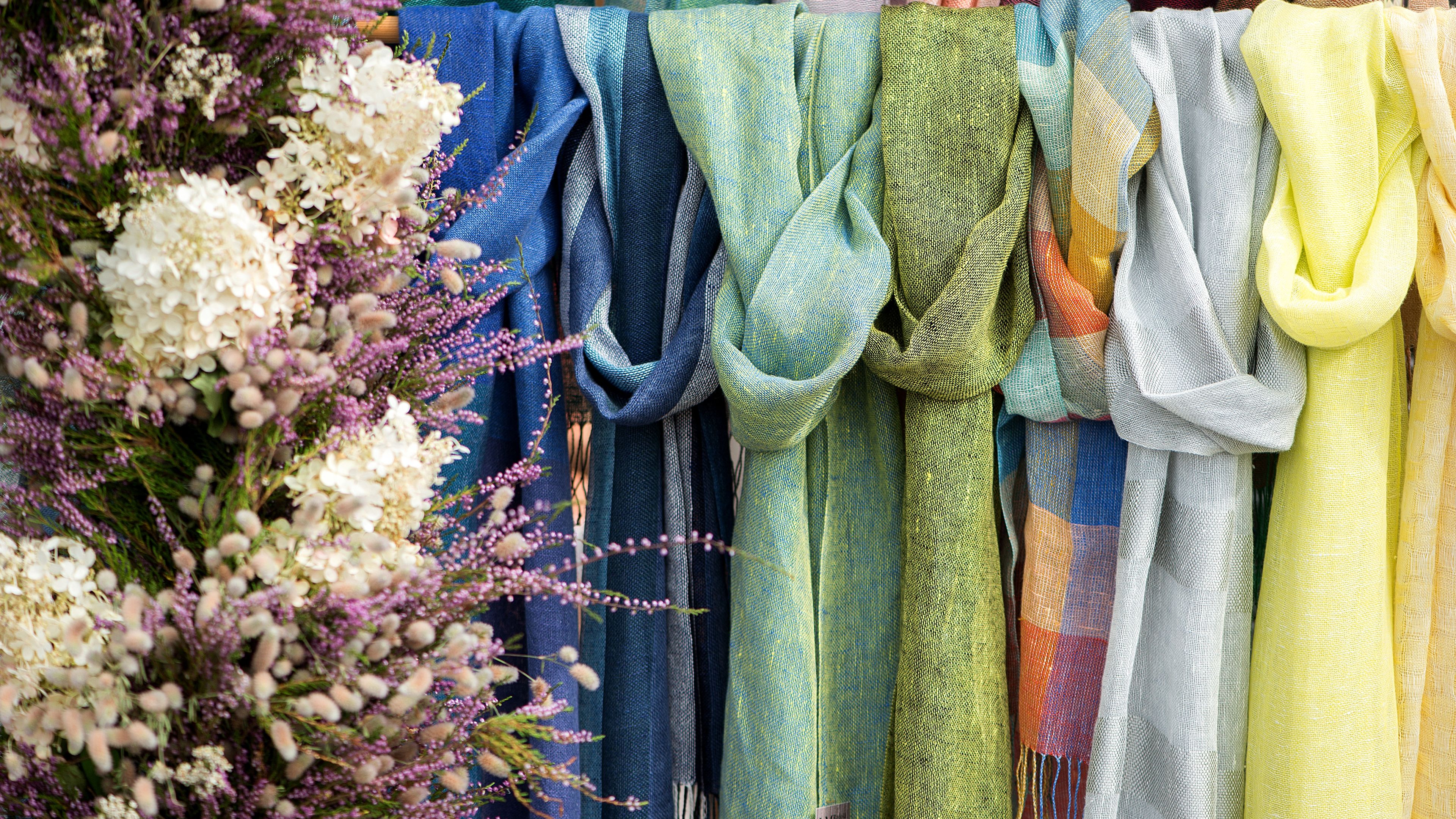 Brightly colored scarves in shades of green, blue, and yellow, hanging neatly on a rack 