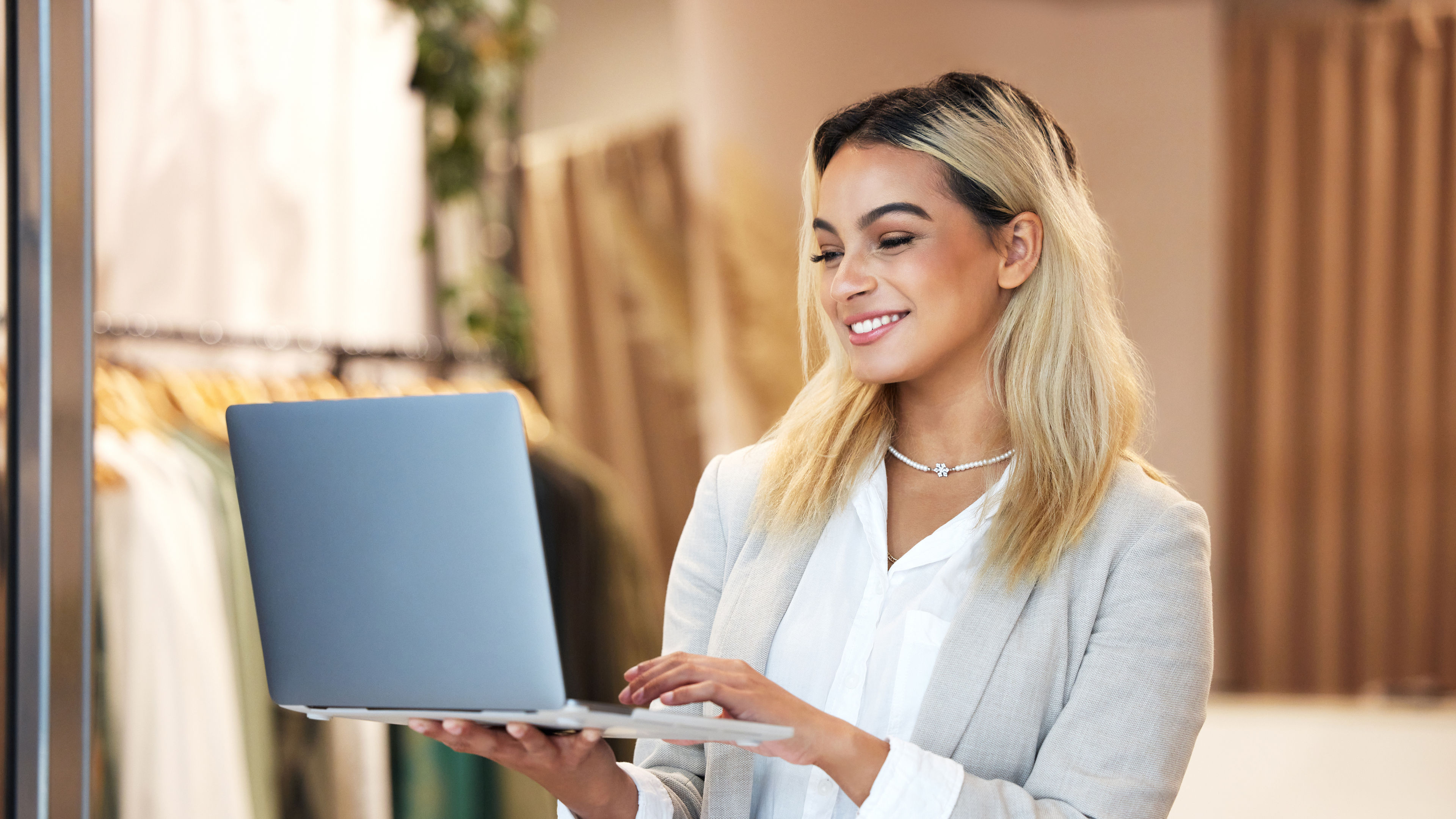 A young business owner sits at a table in her clothing store, using a laptop while surrounded by modern gadgets 