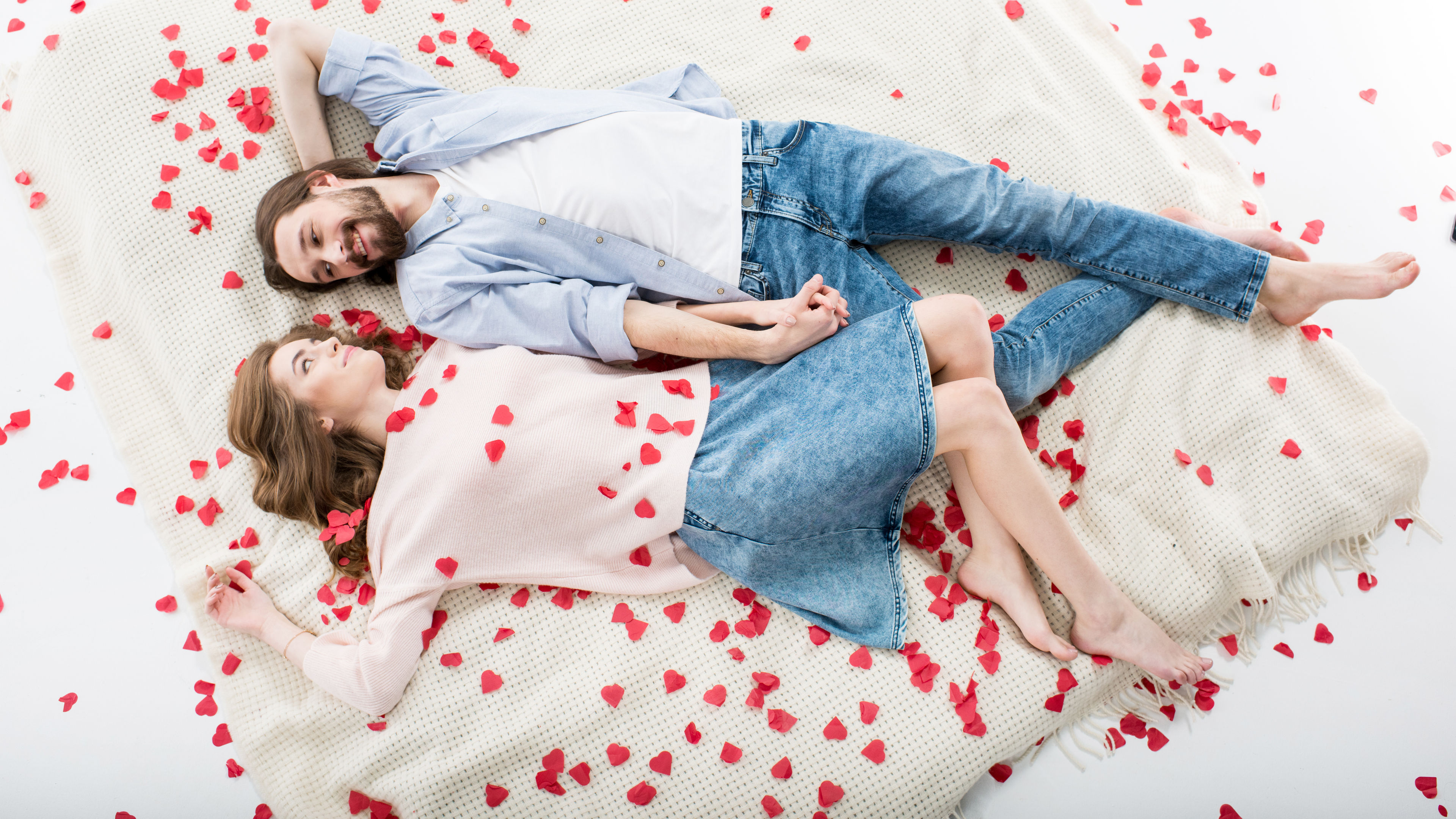 A loving couple lies on a white blanket surrounded by red heart-shaped confetti 