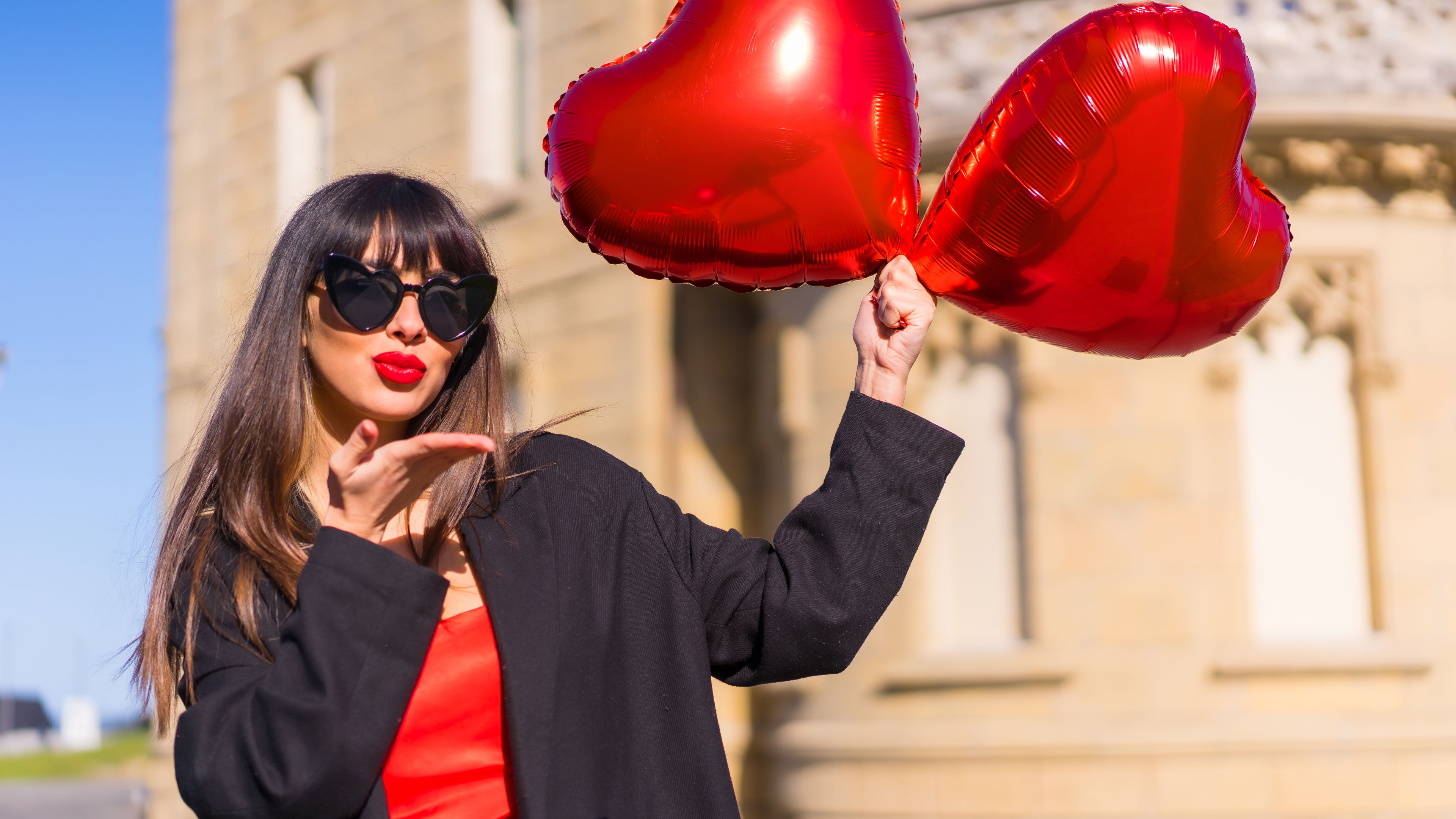 Brunette with heart balloons, sunglasses, and red dress. 