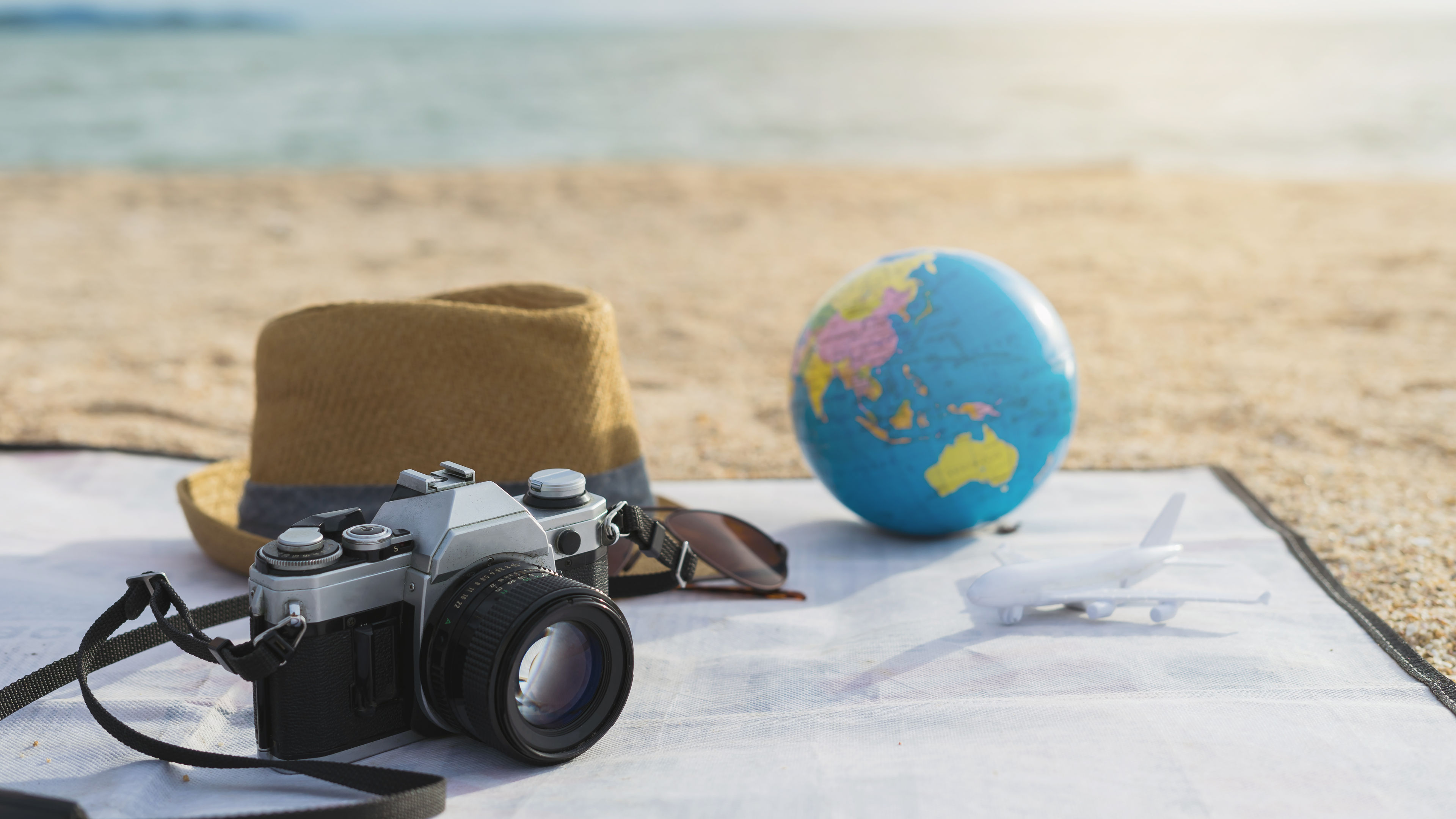 A set of trip essentials like camera, hat etc on a beach 
