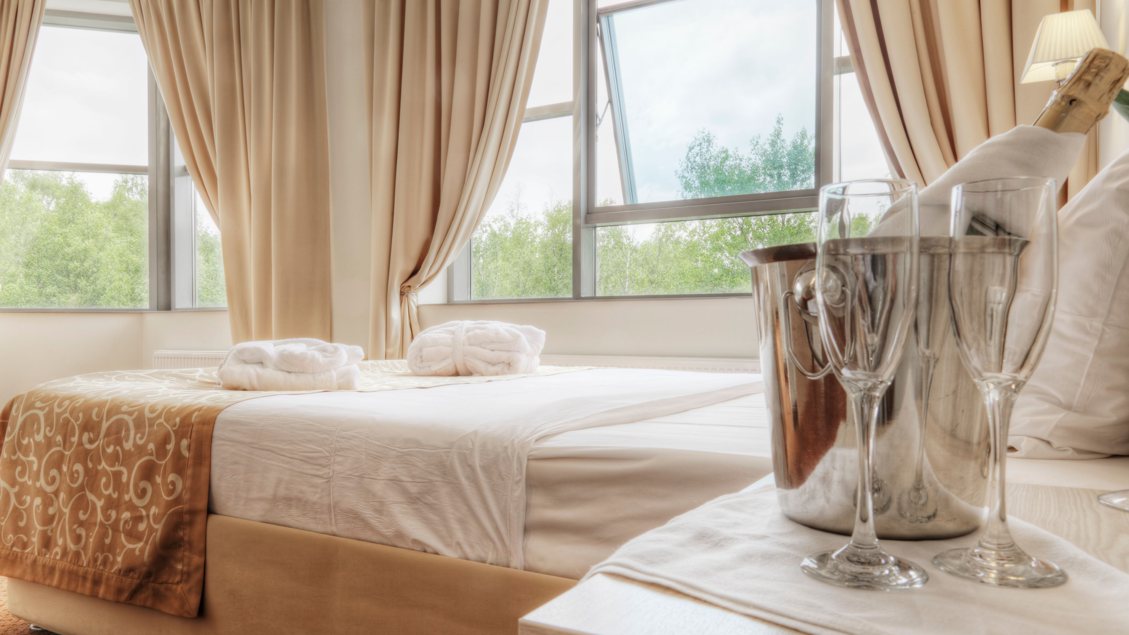 A cozy hotel room with champagne, glasses, and folded robes on a neatly made bed 