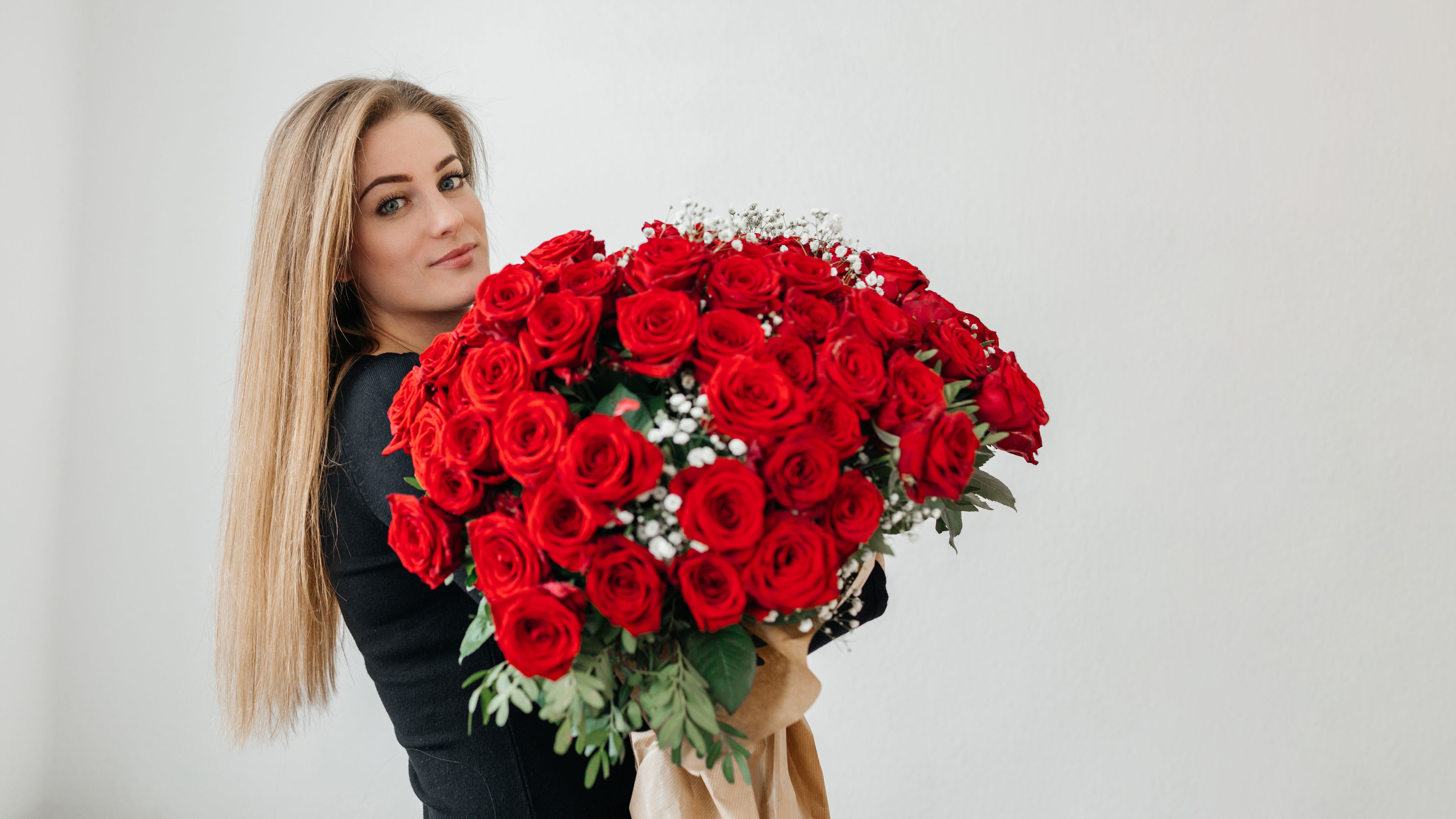 A young woman, dressed in black, holds an enormous bouquet of vibrant red roses 