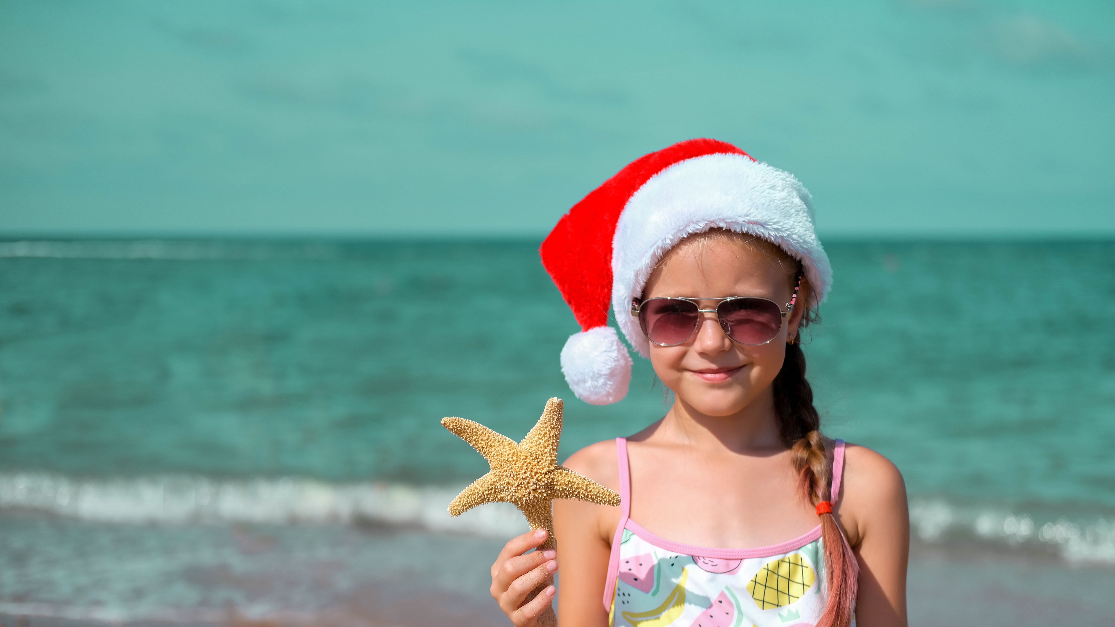 Child on the beach with a Santa hat and starfish. 
