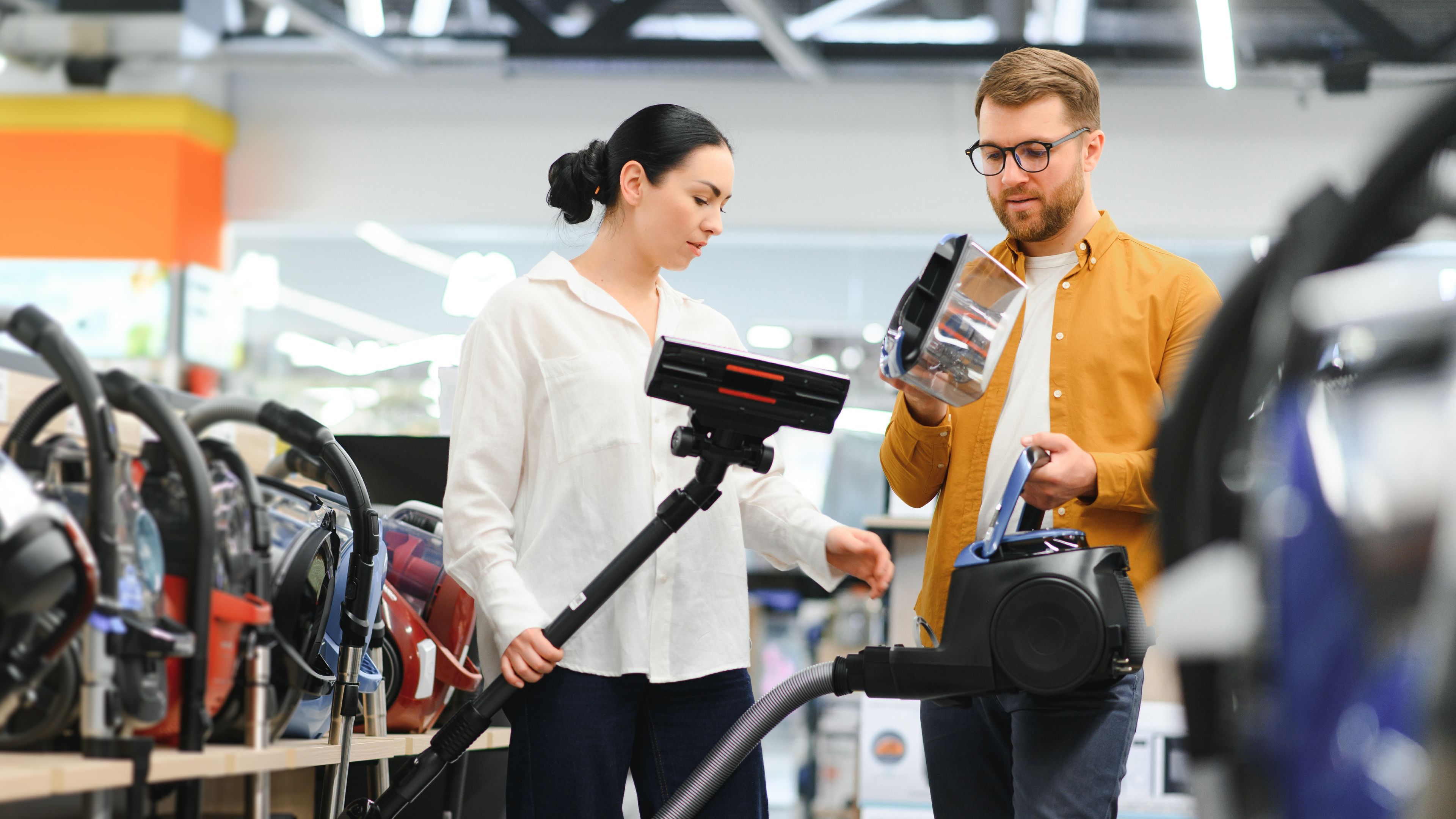 A couple examining a vacuum cleaner in a store, highlighting their quest for the best cleaning solutions 