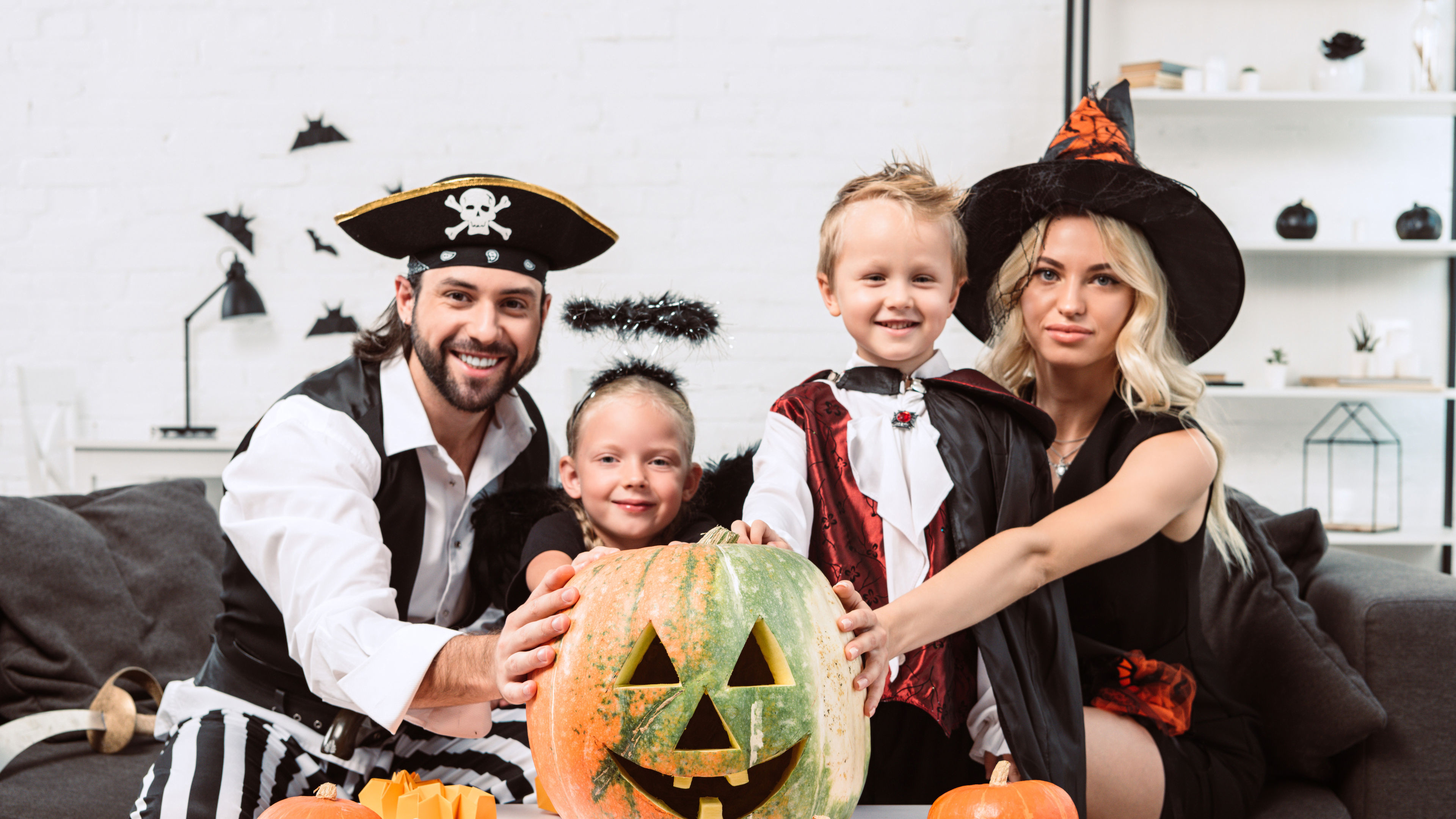 A cheerful family dressed in Halloween costumes, featuring a pirate, witch, and kids, holding a carved pumpkin surrounded by decorations 