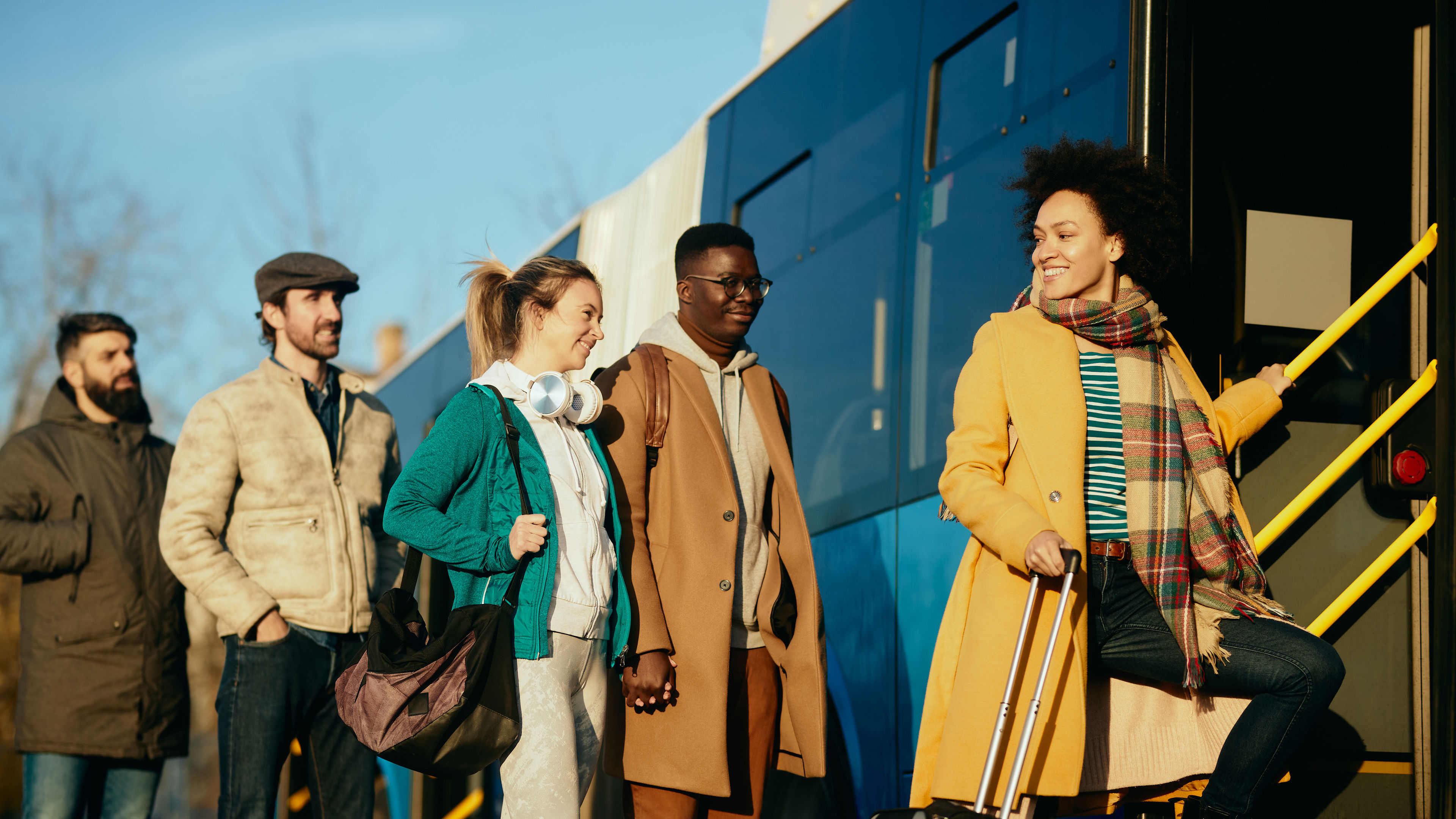 Group of happy people getting in a bus at the station. 