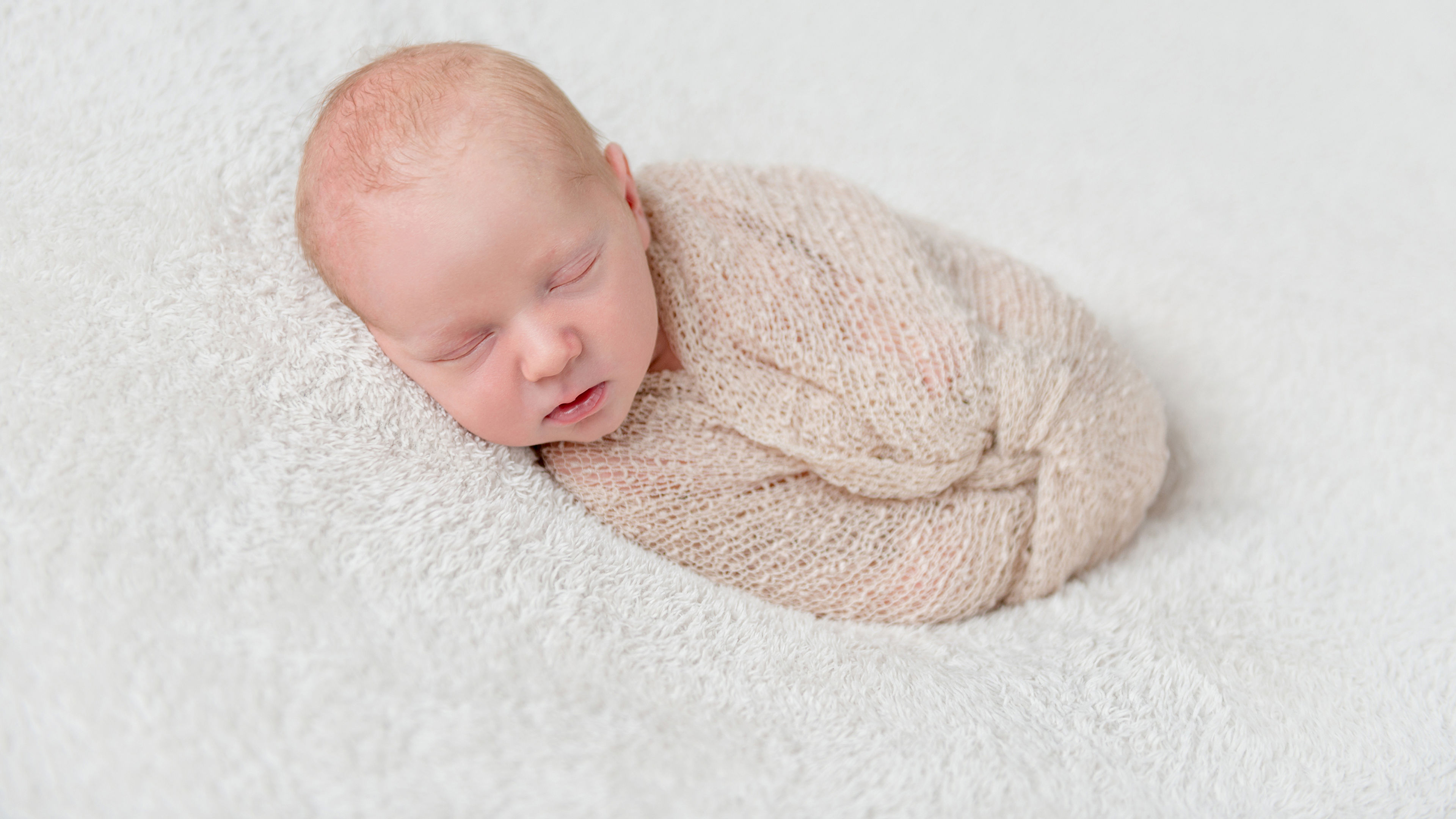 Lovely sleeping baby wrapped in a beige diaper on white blanket. 