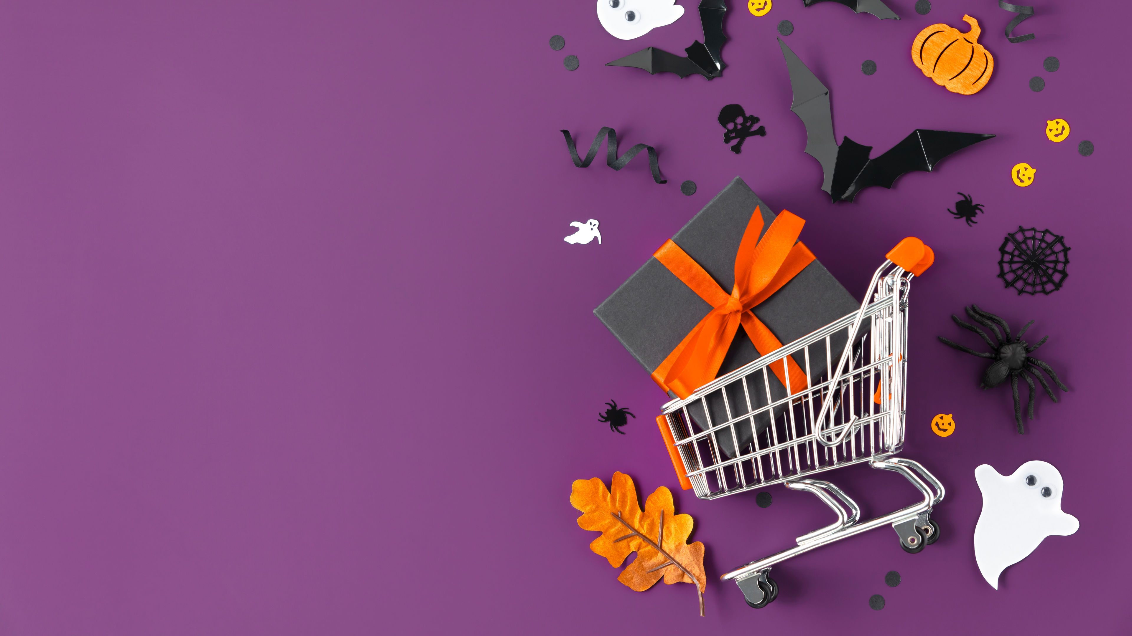 A shopping cart surrounded by Halloween-themed items like ghosts, bats, and pumpkins  