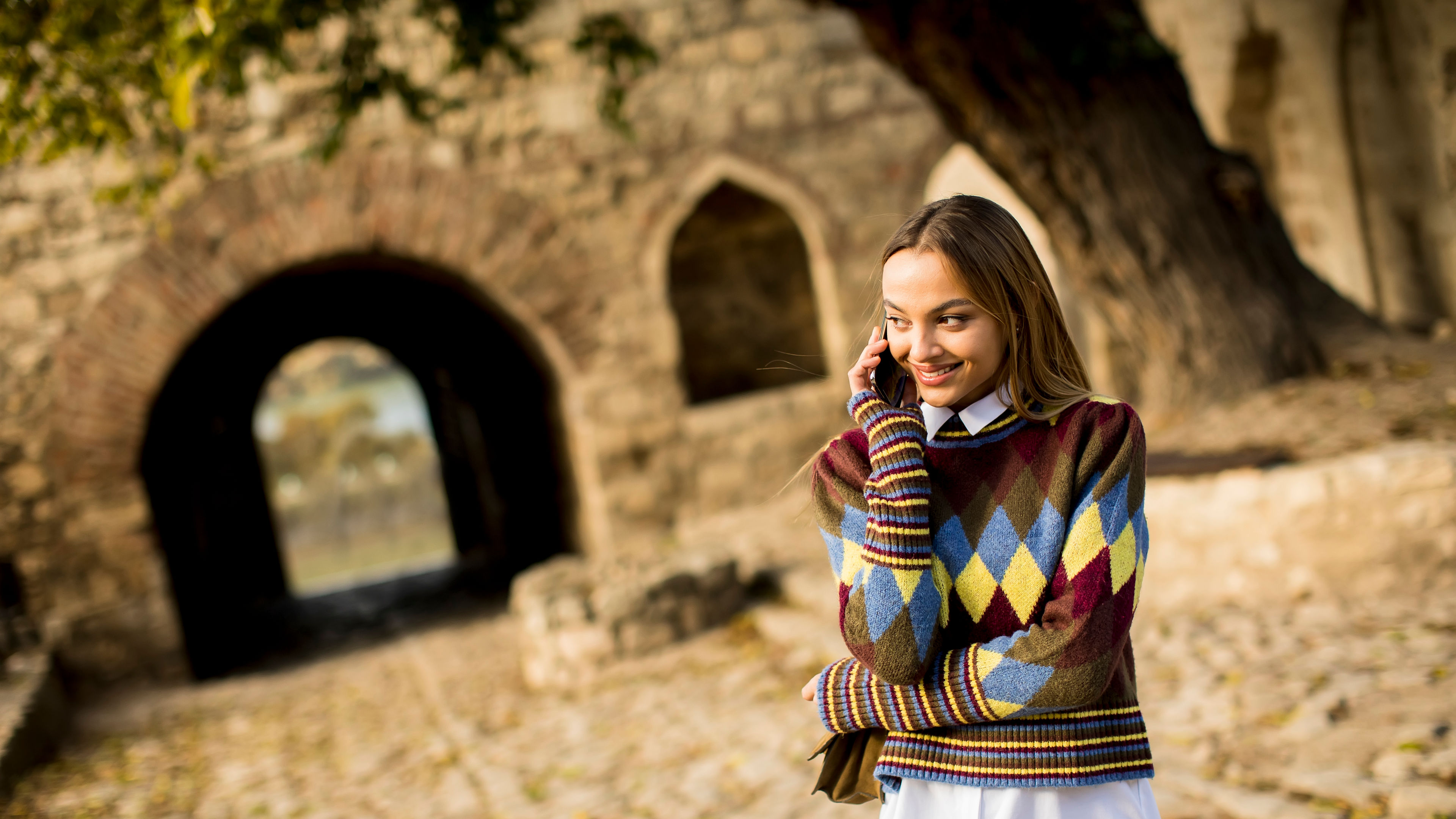 Pretty young woman standing with mobile phone on street at autumn day 