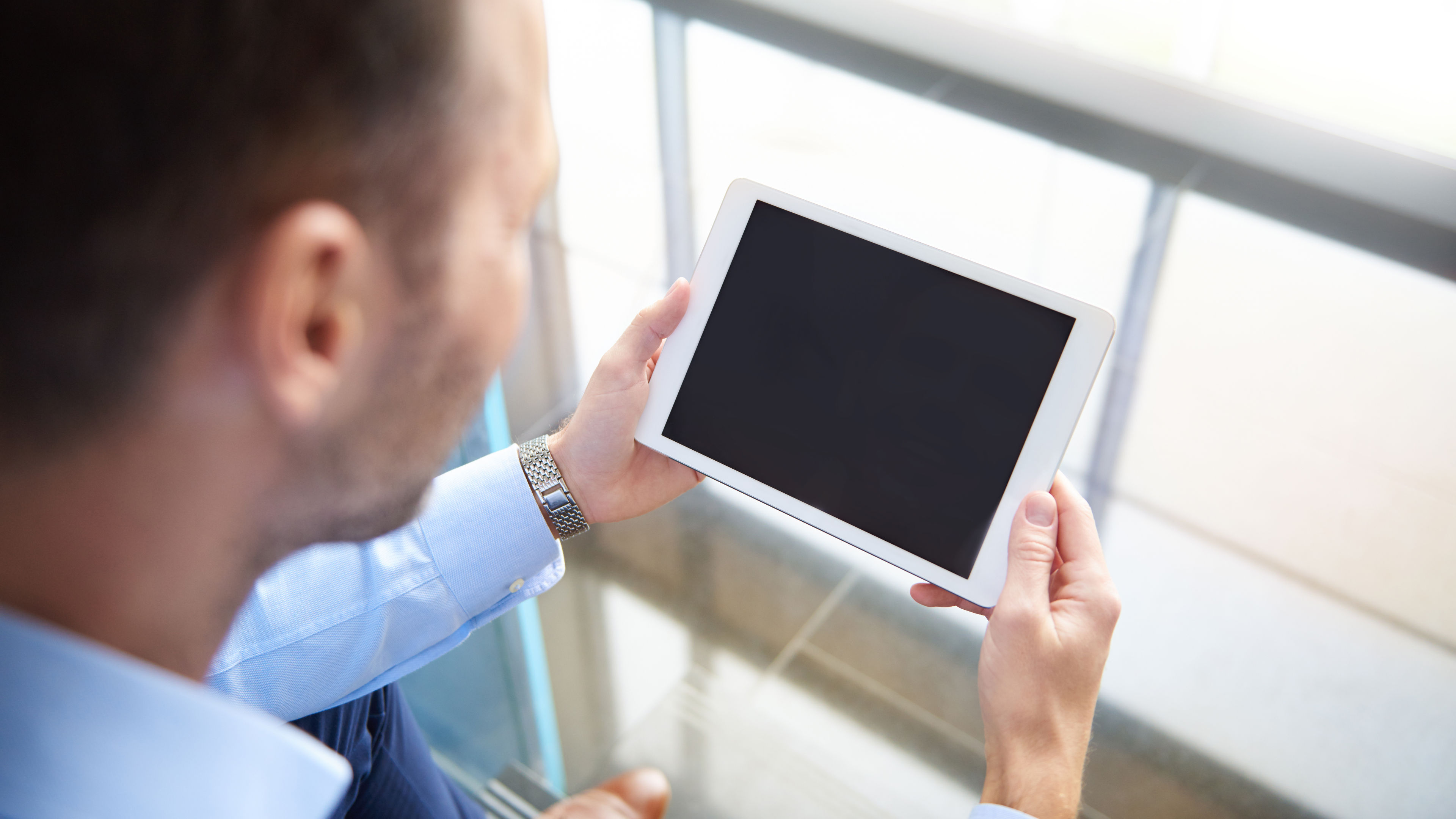 A rear view of a man intently browsing on a digital tablet in a relaxed setting.  