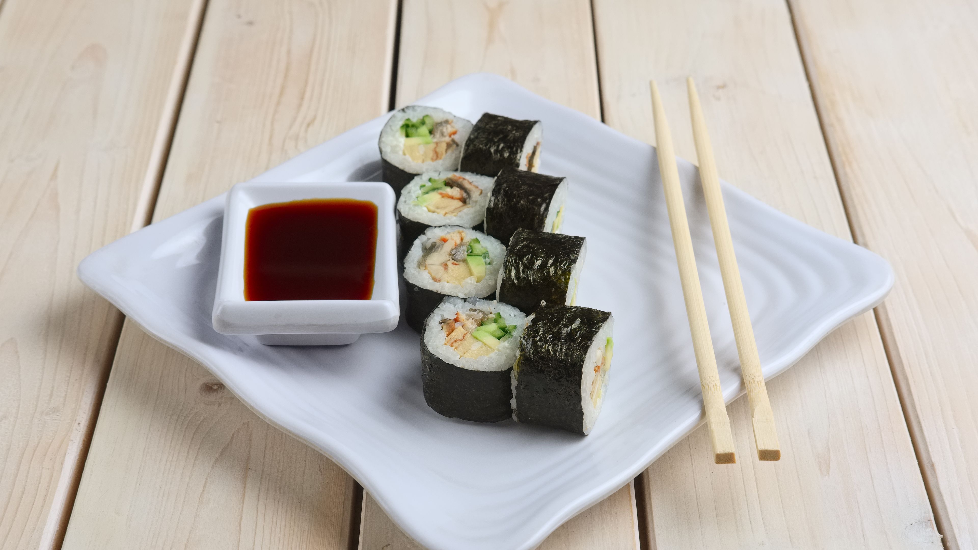 A plate of sushi rolls is served with soy sauce and chopsticks. 