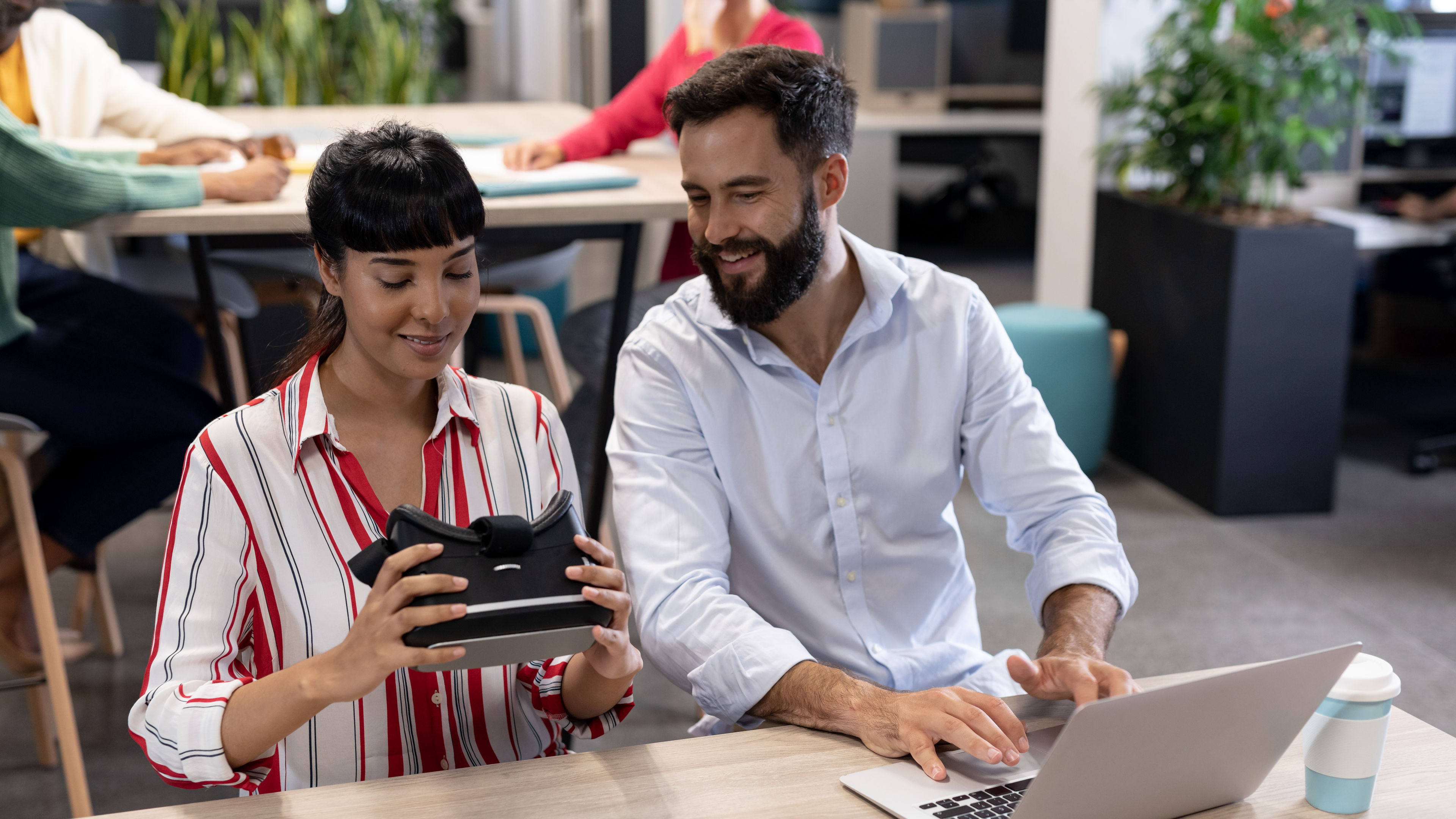 Smiling biracial business colleagues discussing over vr simulator with laptop during meeting 

 