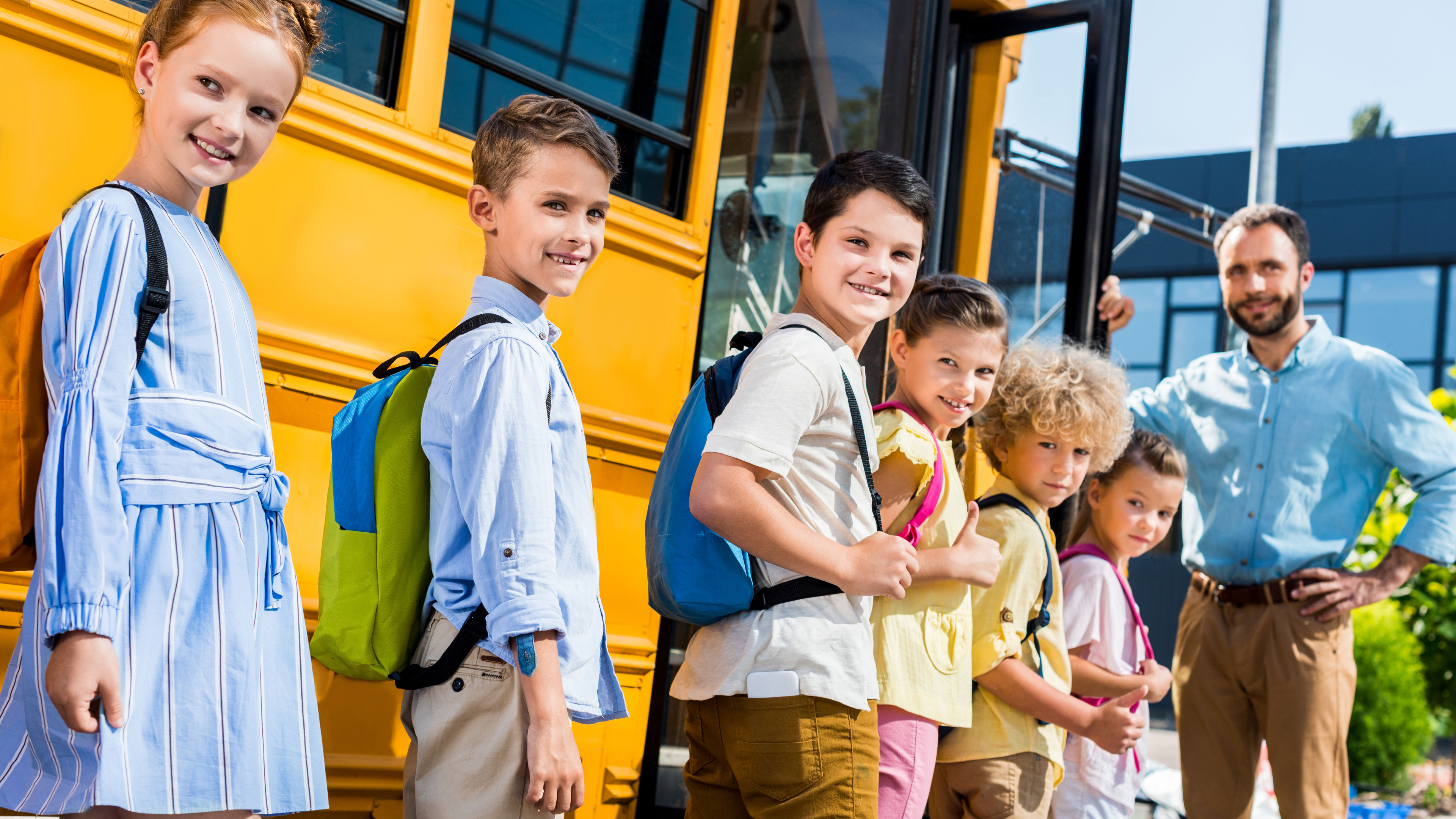 Smiling students with backpacks board a yellow school bus 