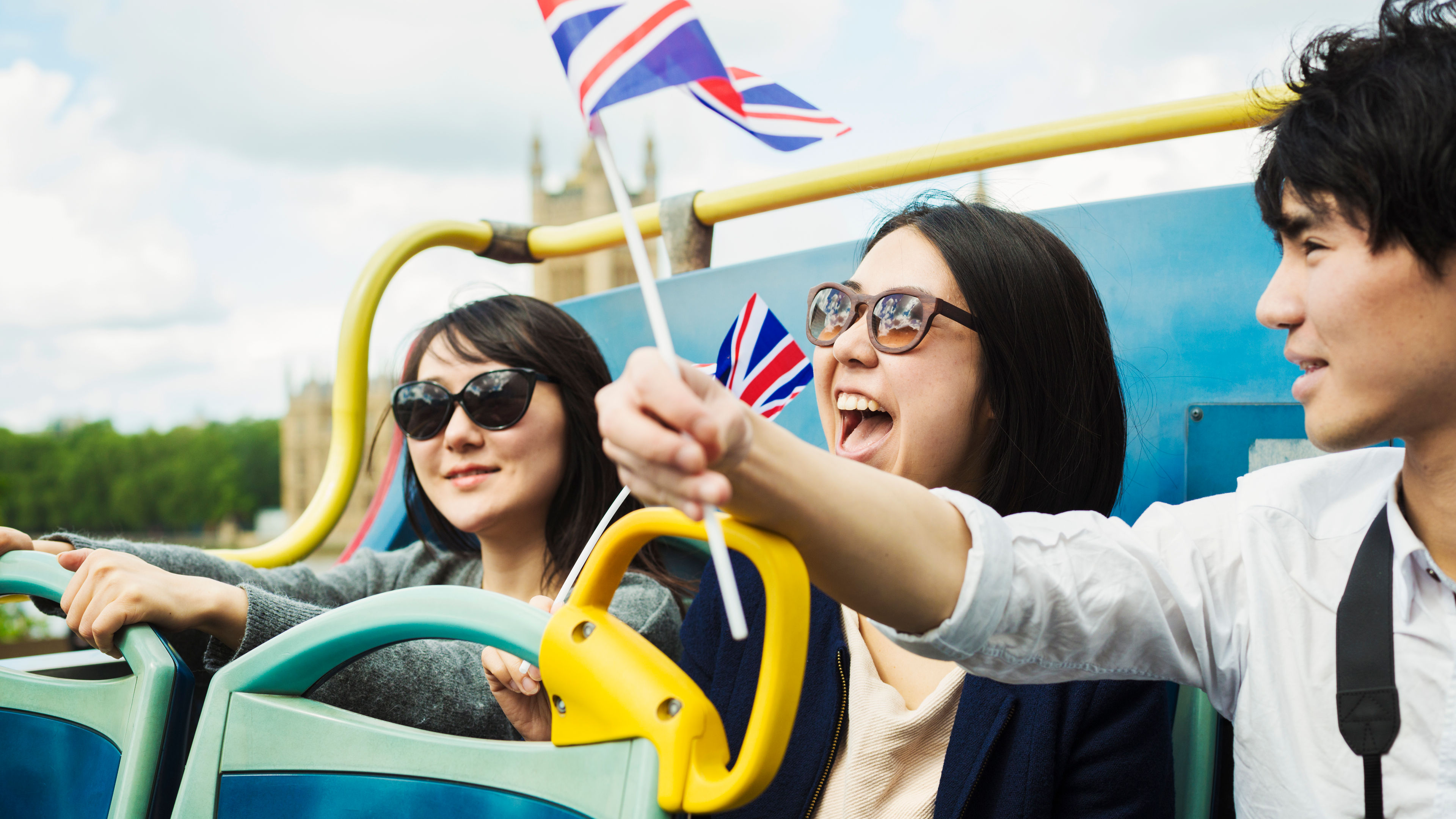 Three tourists waving Union Jack flags on a tour bus 