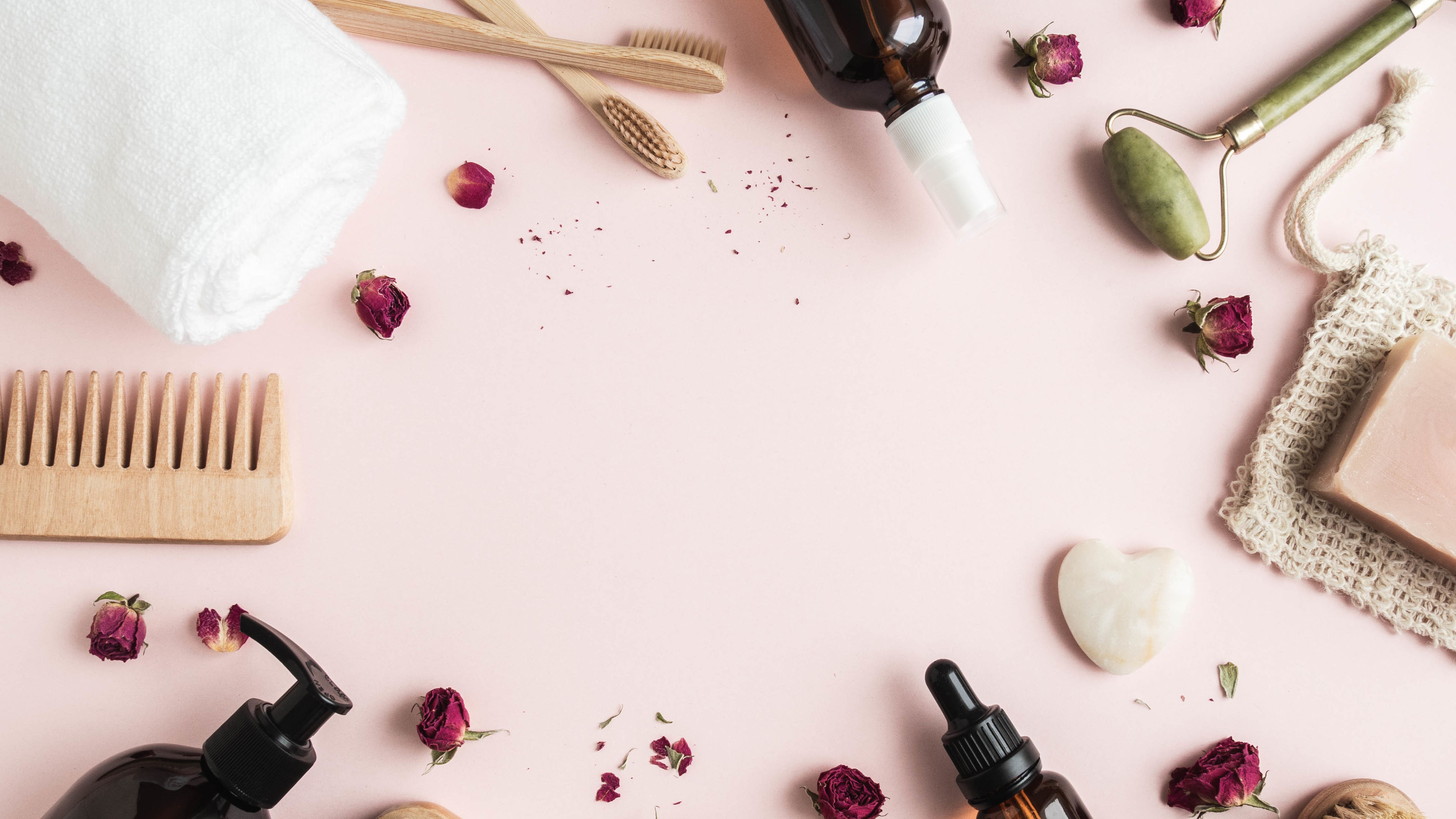 An aesthetically arranged set of self-care items, including wooden combs, brushes, essential oils, a jade roller, and dried rose petals 