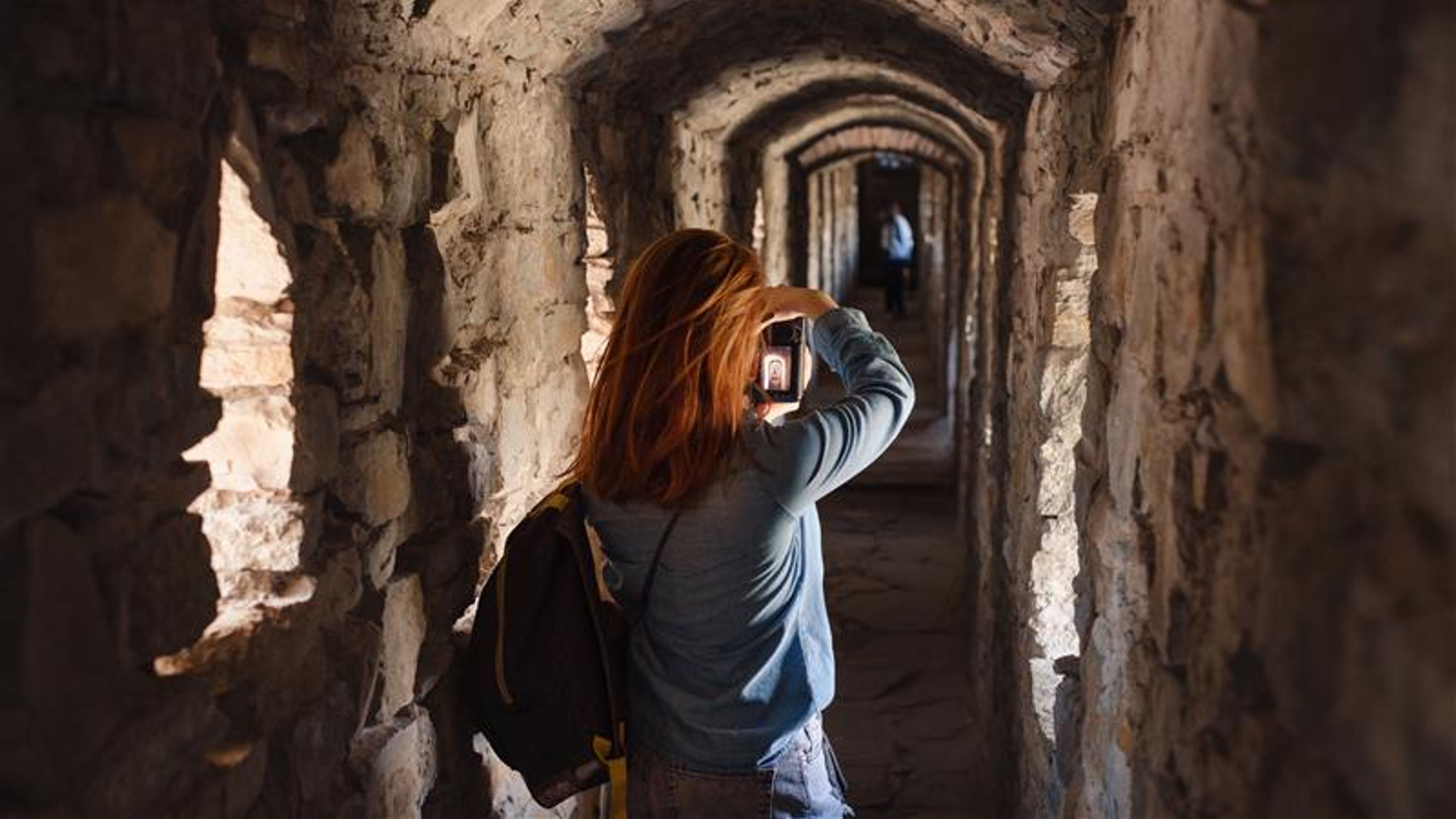 Woman walking through old tunnel, looking in window and taking pictures 