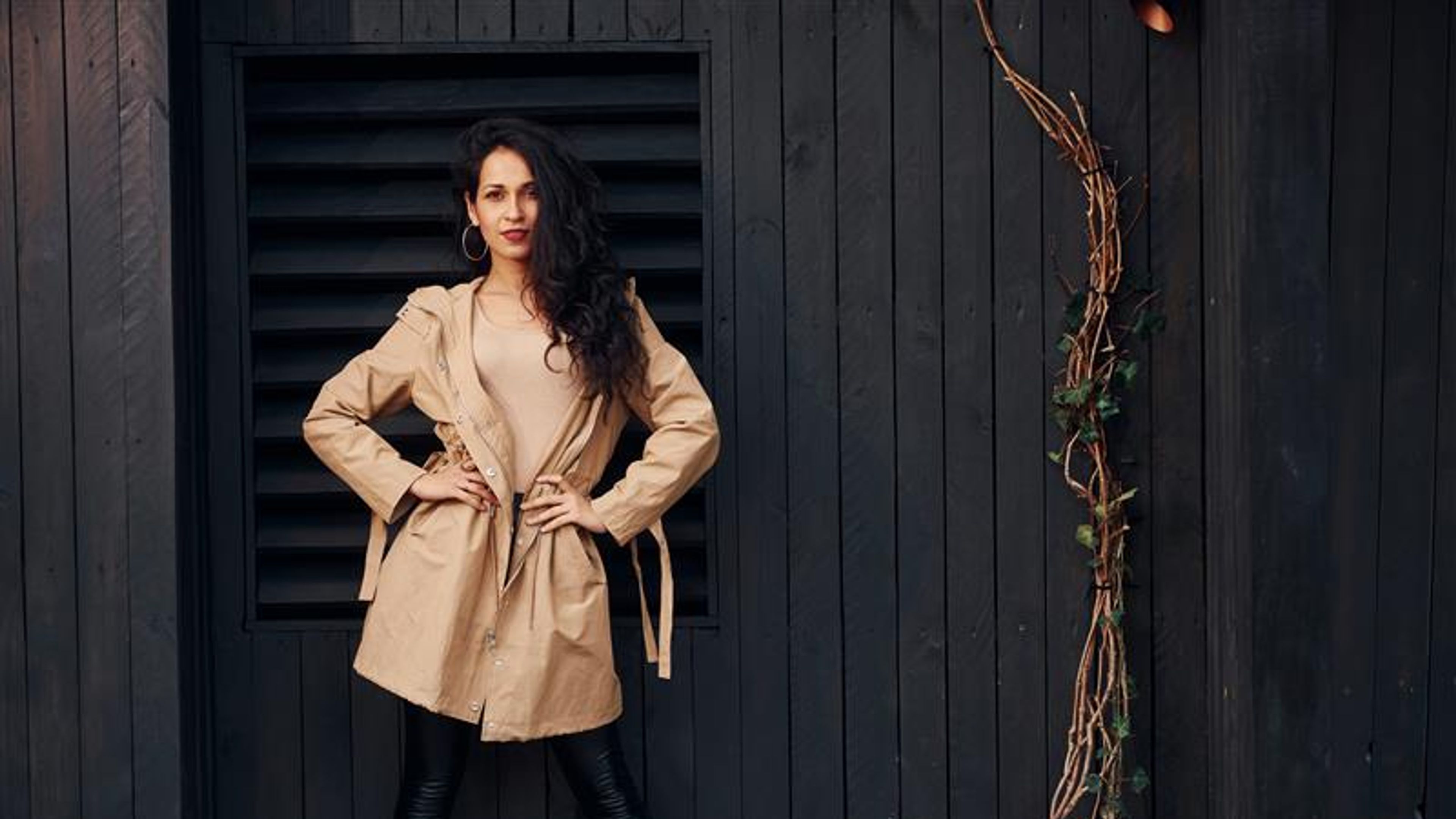 Woman with black curly hair standing against black wooden building exterior 